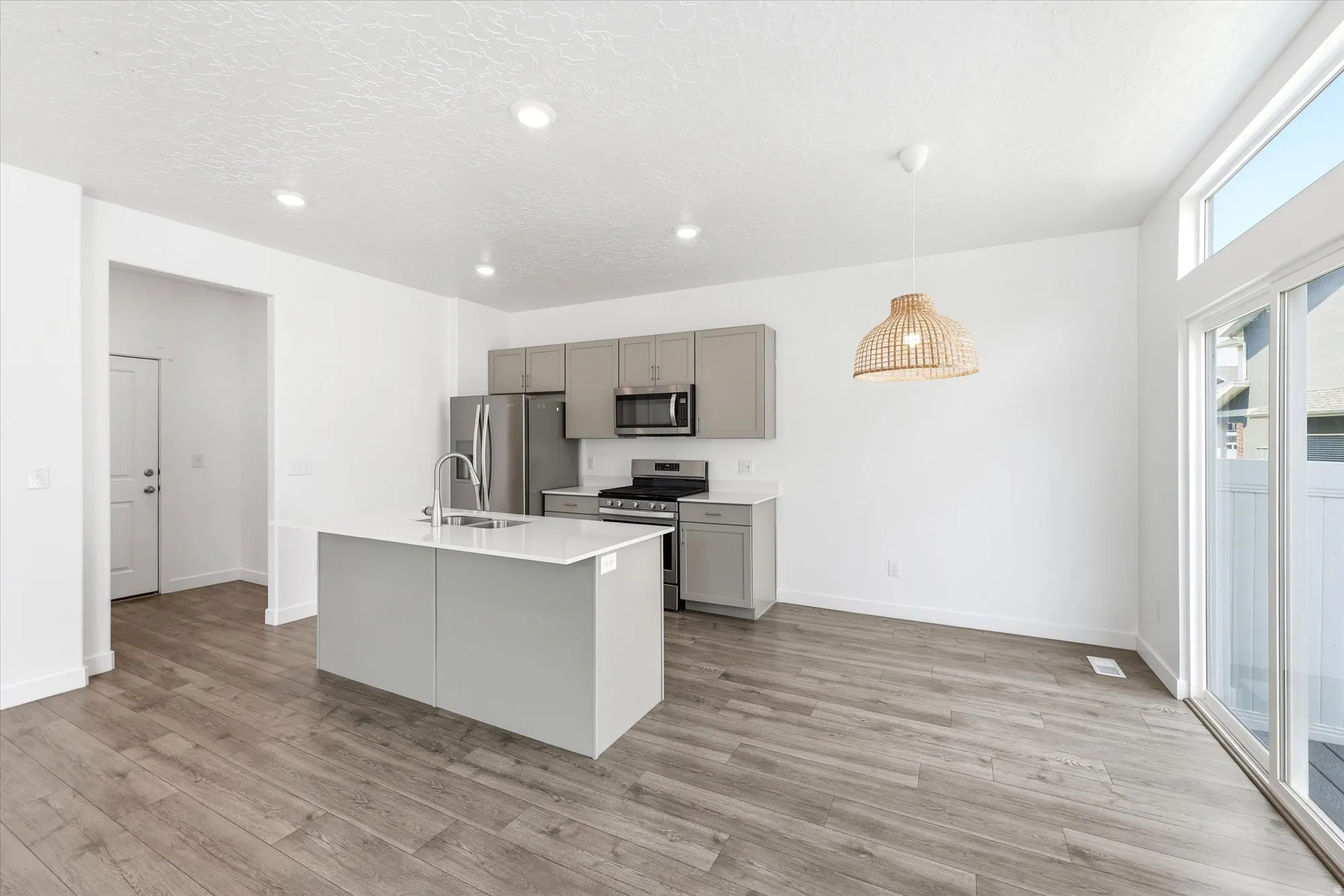 Open-concept kitchen and dining area featuring wood-finish flooring, recessed lighting, and a kitchen island with an integrated sink