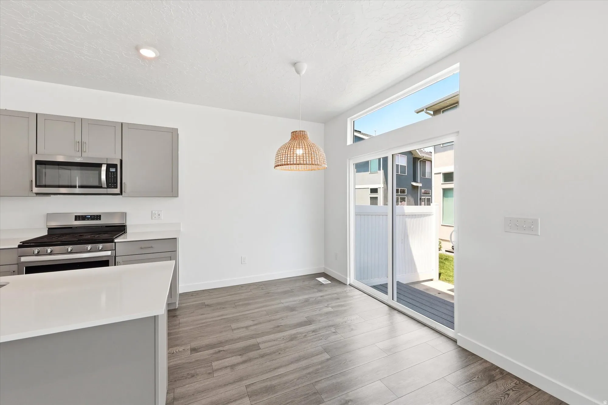 Modern kitchen and dining area featuring light gray cabinetry, stainless steel appliances, and white countertops