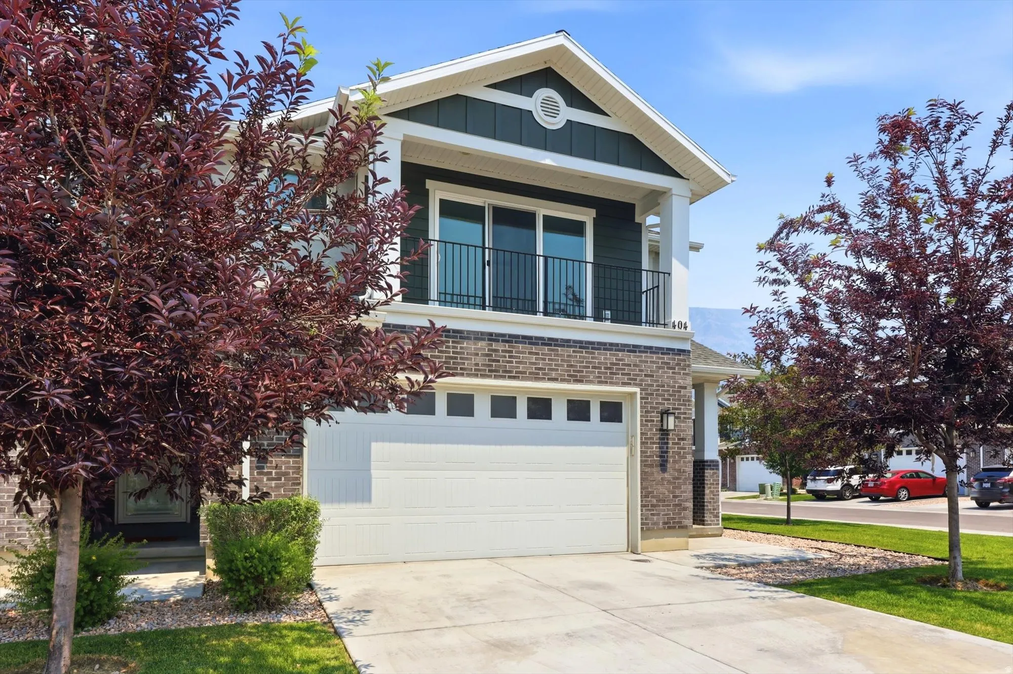 Two-story residence featuring brick and dark siding accents, a prominent front-facing gable, and an upper-level balcony with black railing