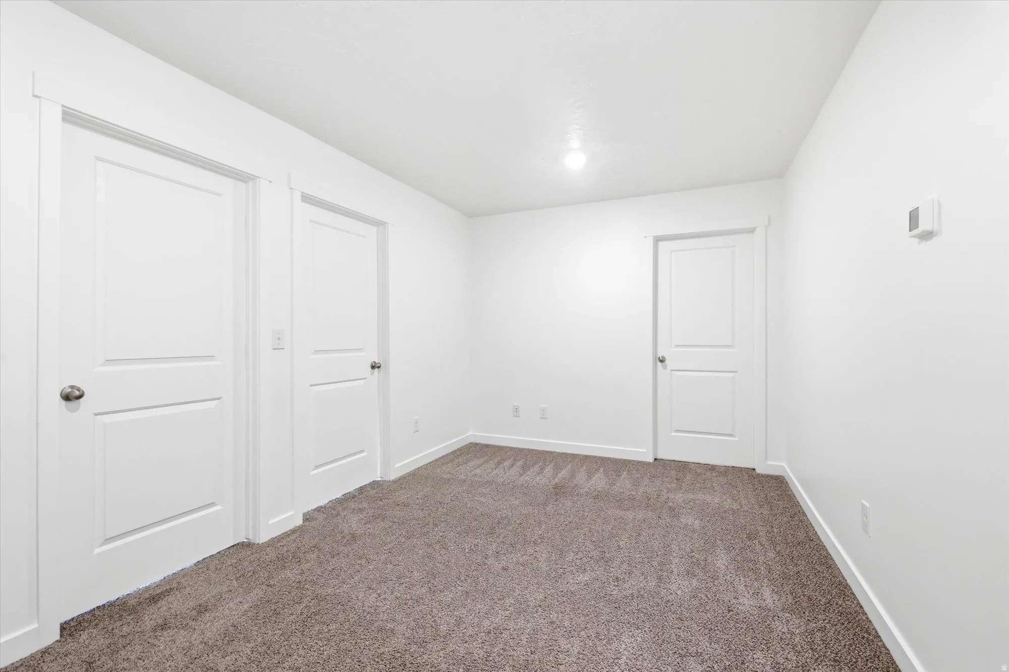 Room featuring plush grey carpet, white walls, and bright overhead lighting