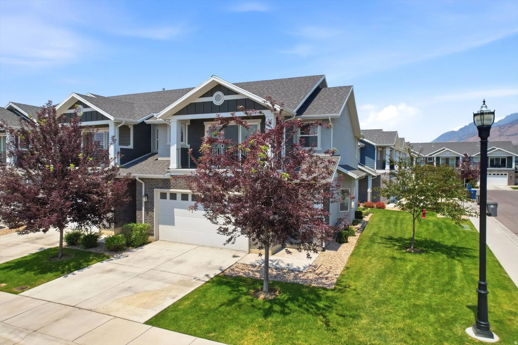 Modern townhome exterior featuring a two-car garage, concrete driveway, and front lawn
