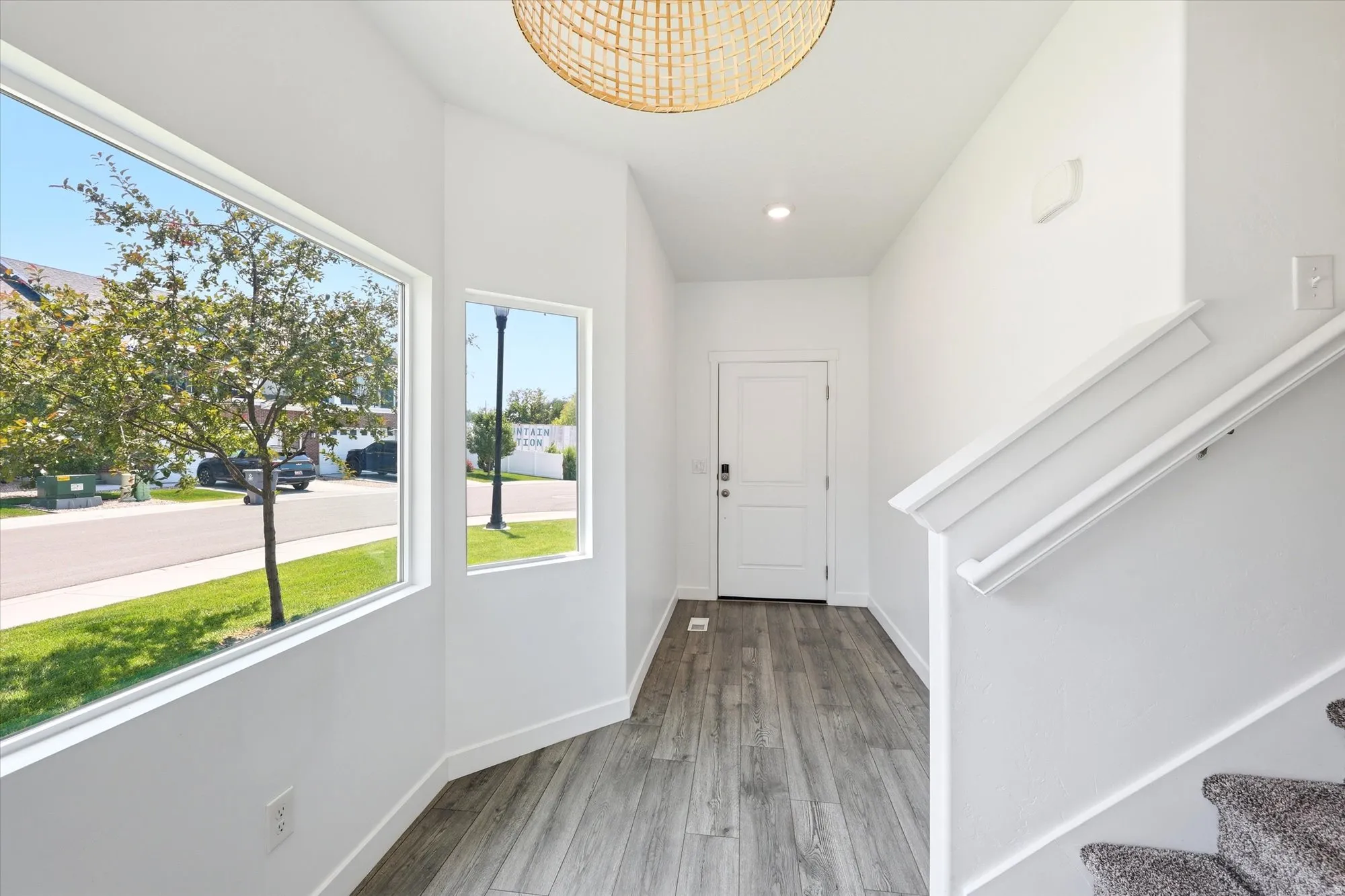 Entryway featuring expansive windows, wood-finish flooring, a white paneled door with smart lock, a rattan-style overhead light fixture, and a carpeted staircase with white handrail