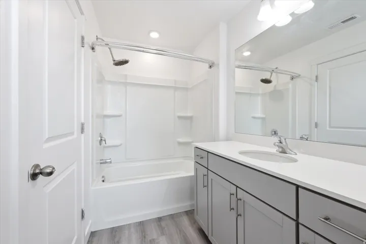 Full bathroom featuring a white tub/shower combination, light gray wood-finish flooring, a white countertop vanity with gray cabinetry, an integrated sink, and a large wall-mounted mirror