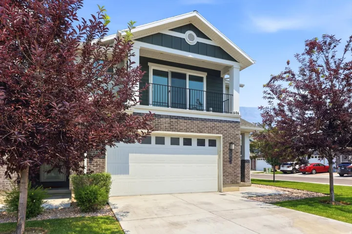 Two-story residence featuring brick and dark siding accents, a prominent front-facing gable, and an upper-level balcony with black railing