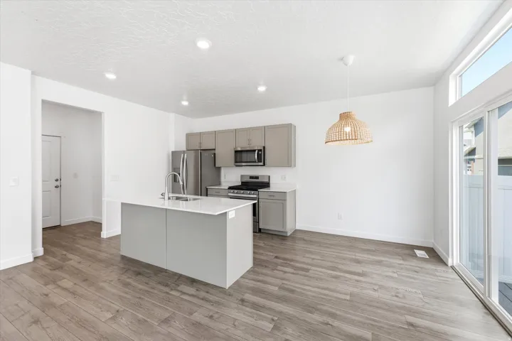 Open-concept kitchen and dining area featuring wood-finish flooring, recessed lighting, and a kitchen island with an integrated sink
