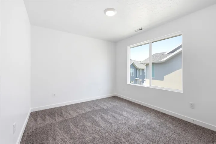 Bright room with a large window, neutral gray carpet, white walls, and a ceiling-mounted light fixture