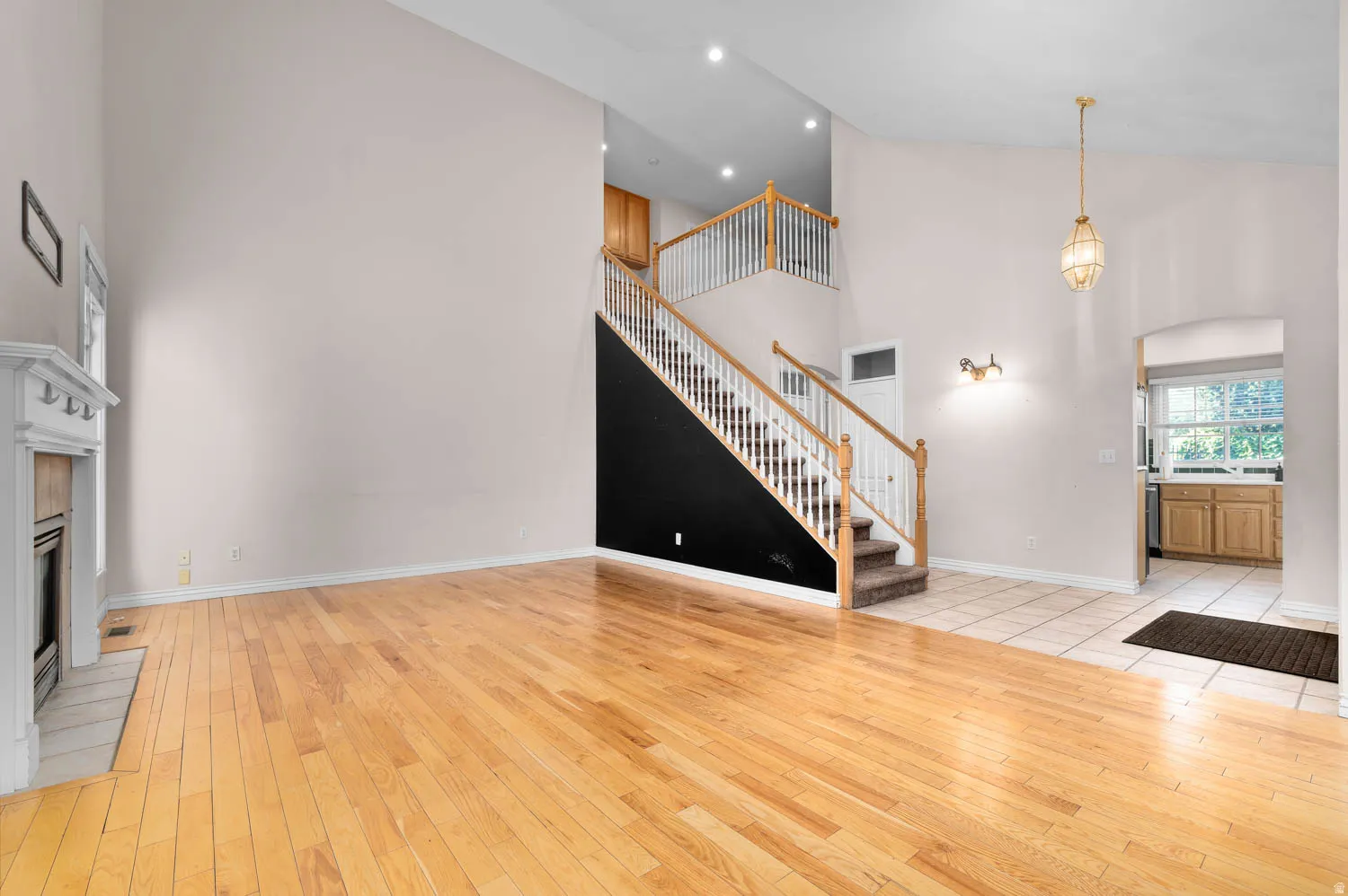 Spacious living area featuring wood-finish flooring, a white mantel fireplace, vaulted ceilings, and a two-story staircase with a wood handrail and white balusters