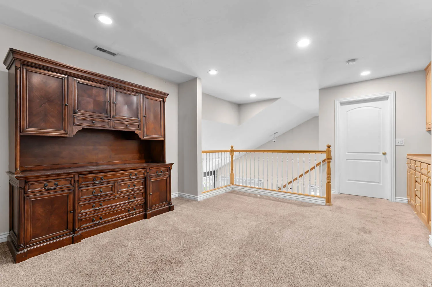 Spacious carpeted upper-level area featuring recessed lighting, a built-in wood hutch with patterned details, and a light wood railing