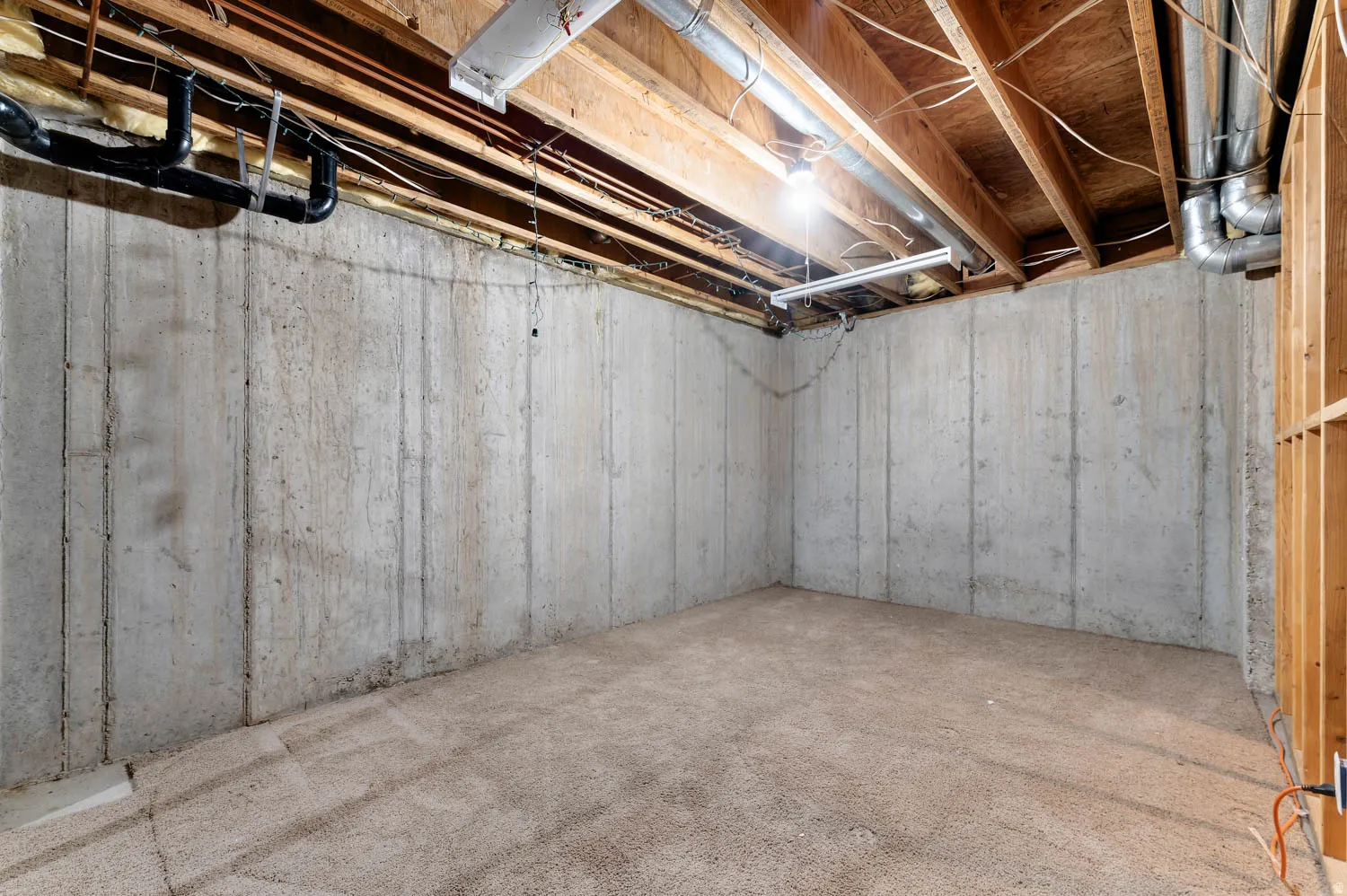 Unfinished basement featuring exposed wood ceiling joists and concrete walls, with visible plumbing and ductwork