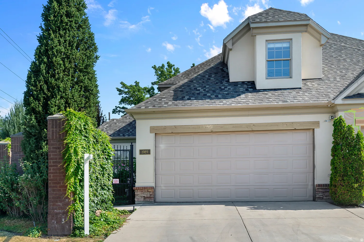 Cream-colored garage door with a light wood-finish lintel, stone veneer accents, and a dormer window above