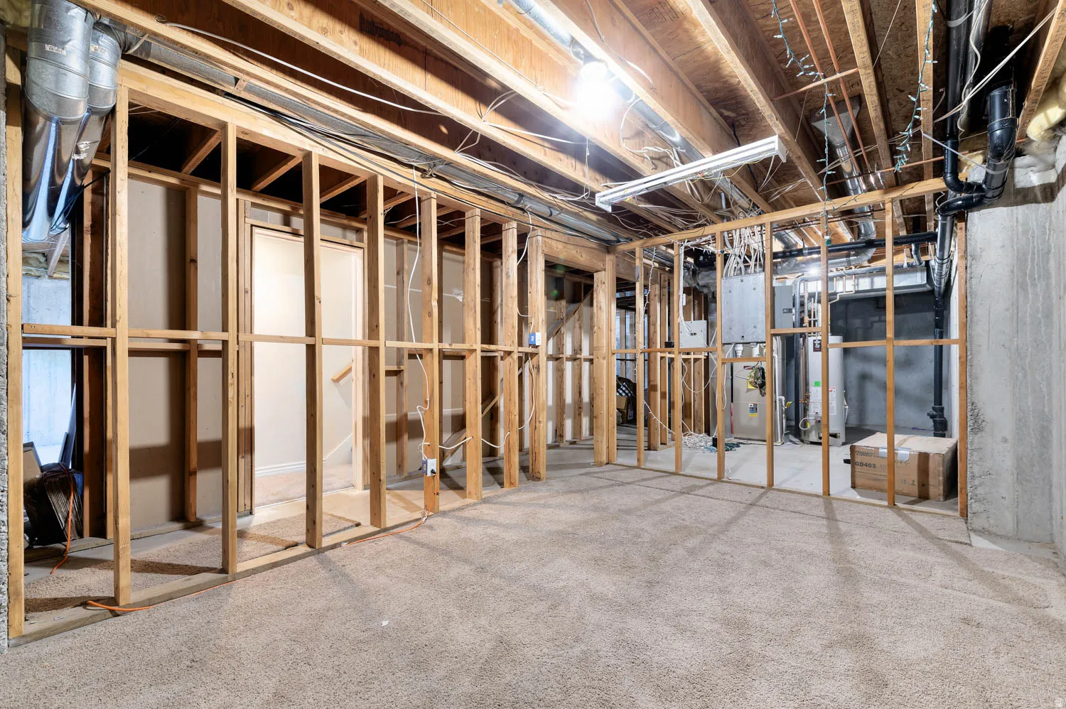 Unfinished basement featuring wood framing, exposed ceiling joists, utility access, and a carpeted floor