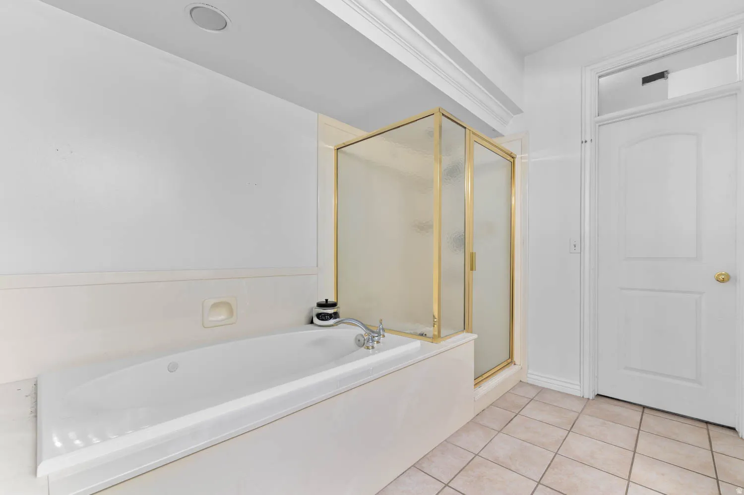 Spacious bathroom featuring a built-in soaking tub, a shower enclosure with gold-tone framing, white walls, crown molding, and tiled flooring