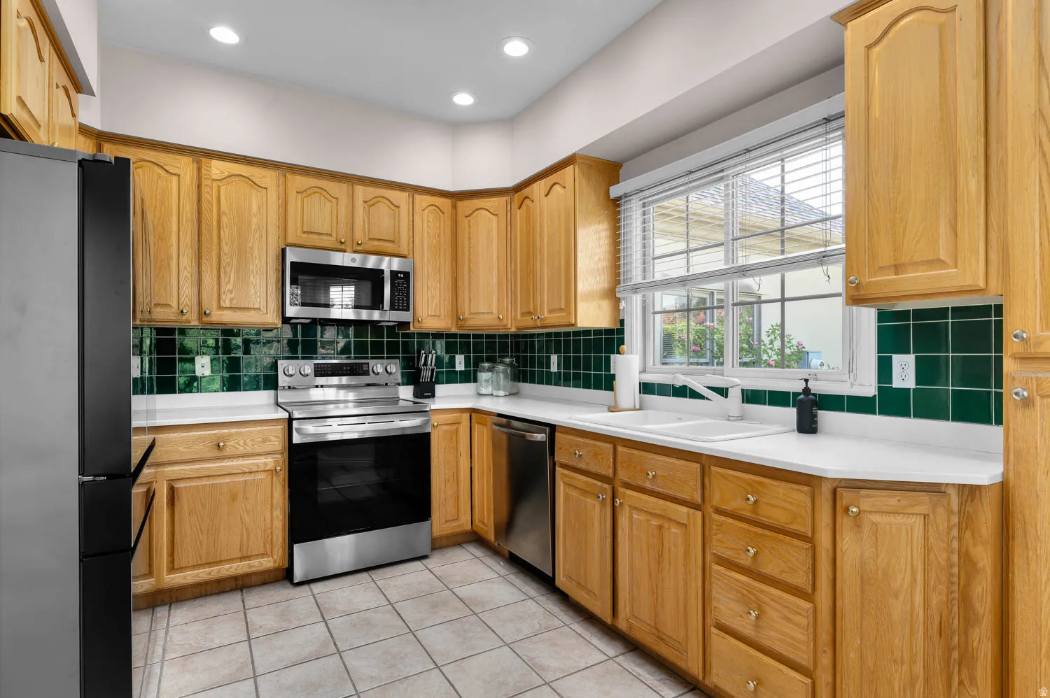 Kitchen featuring natural wood cabinetry, white countertops, stainless steel appliances, a green tile backsplash, and recessed lighting