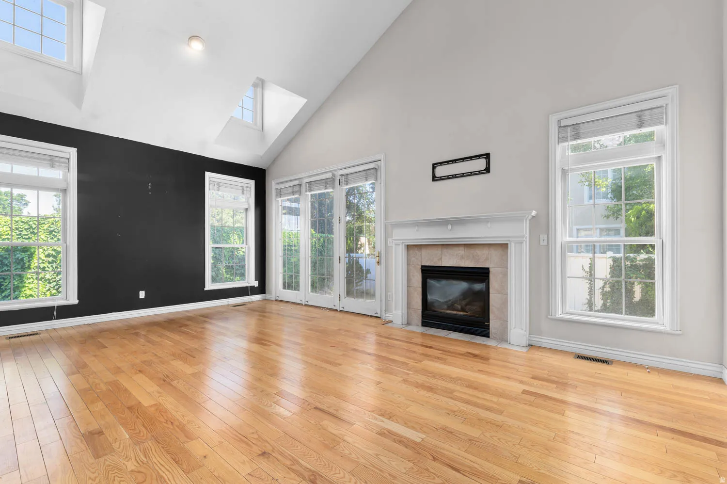 Spacious interior featuring hardwood flooring, a vaulted ceiling, a fireplace with a mantel, skylights, and French doors