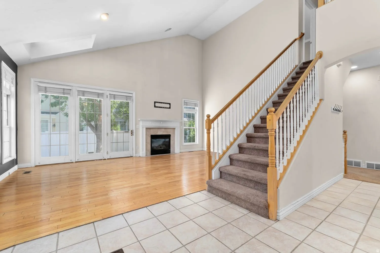 Vaulted ceiling living area featuring a fireplace with a mantel, wood-finish flooring, and expansive glass doors