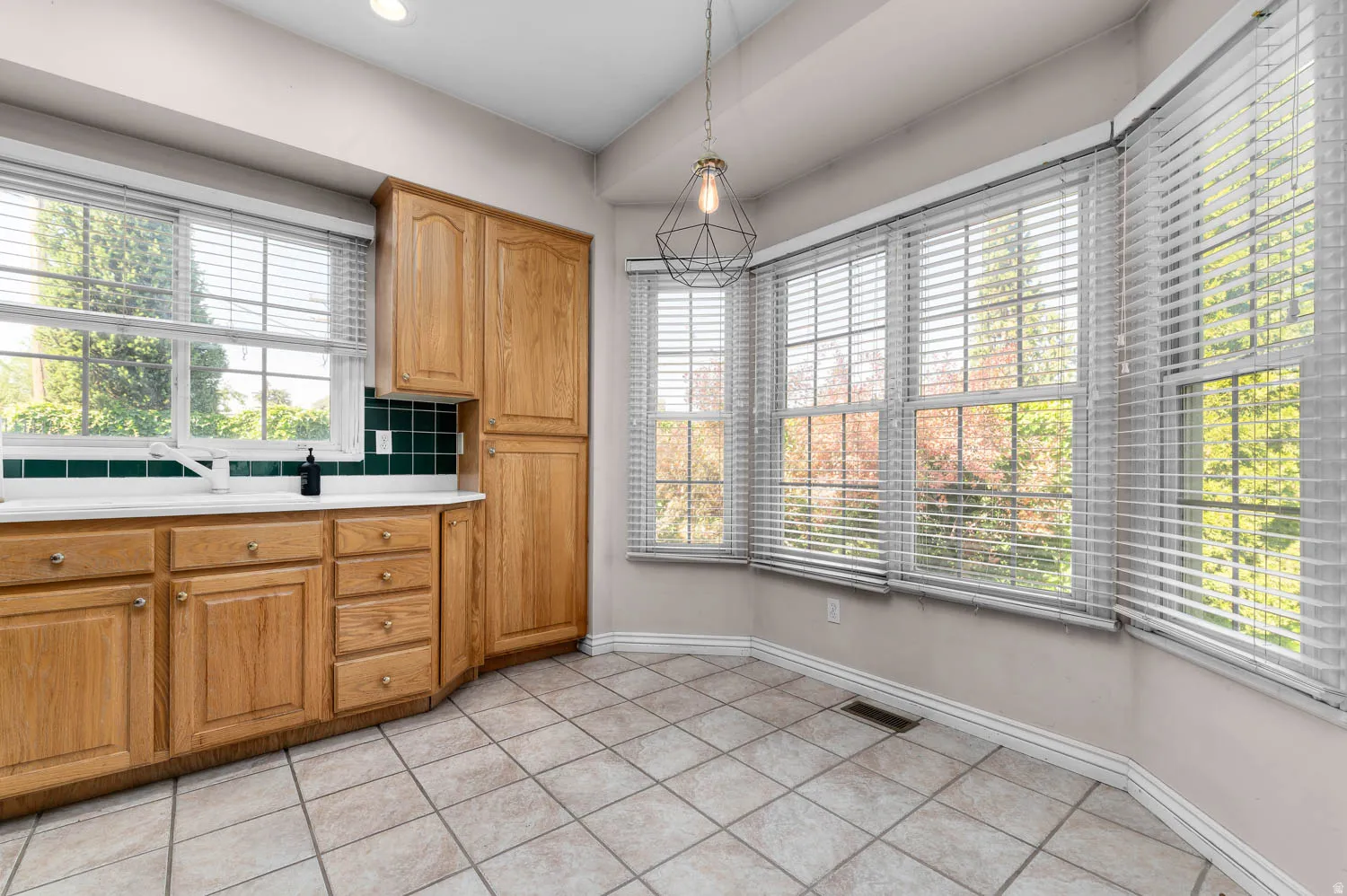 Kitchen area featuring natural wood cabinetry, white countertops, and a green tile backsplash