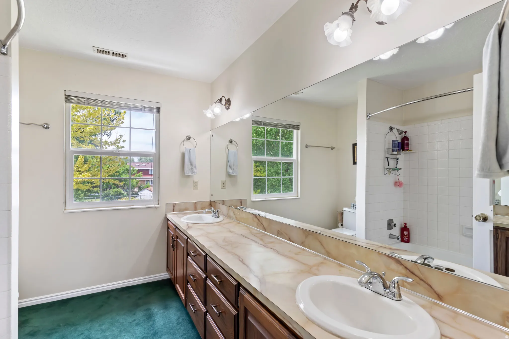 Bathroom featuring a dual vanity with a patterned countertop, wood-finish cabinetry, and an oversized mirror