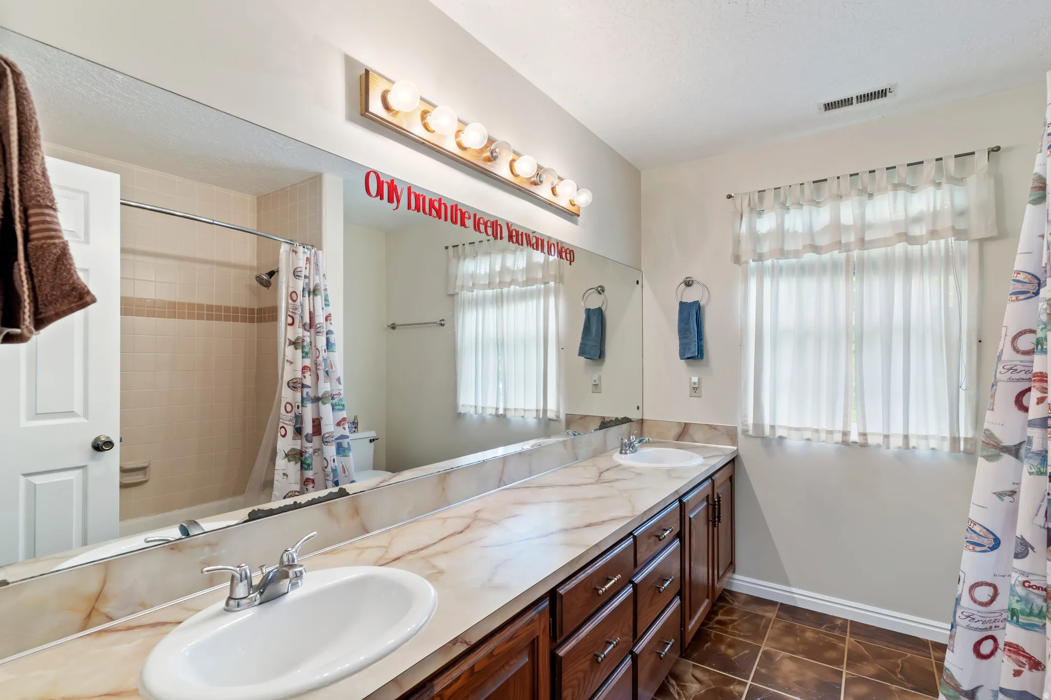 Bathroom featuring a long dual vanity with a patterned countertop, dual undermount sinks, and dark wood cabinetry