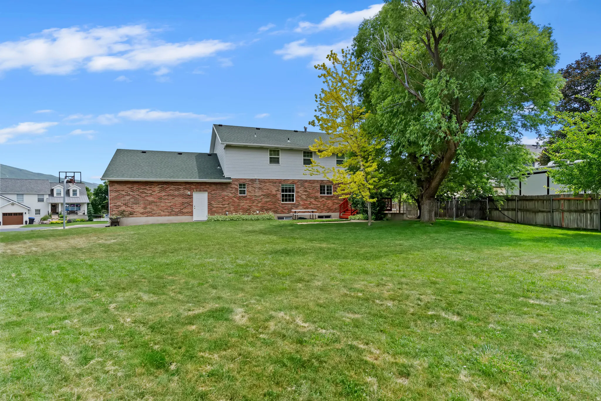 Expansive grass yard with mature trees and a wood fence