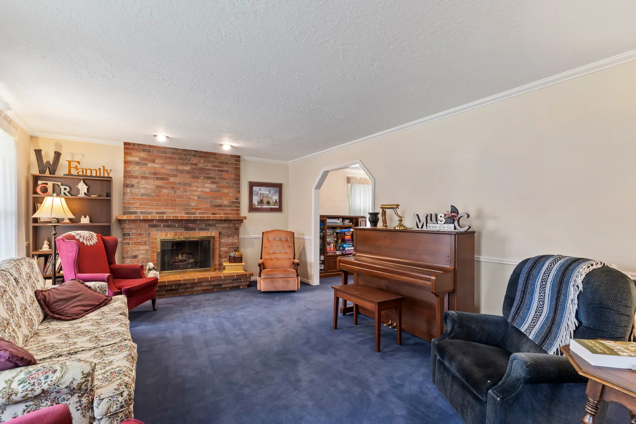 Living area featuring a brick fireplace, built-in shelving, crown molding, a recessed lighting fixture, and an arched doorway