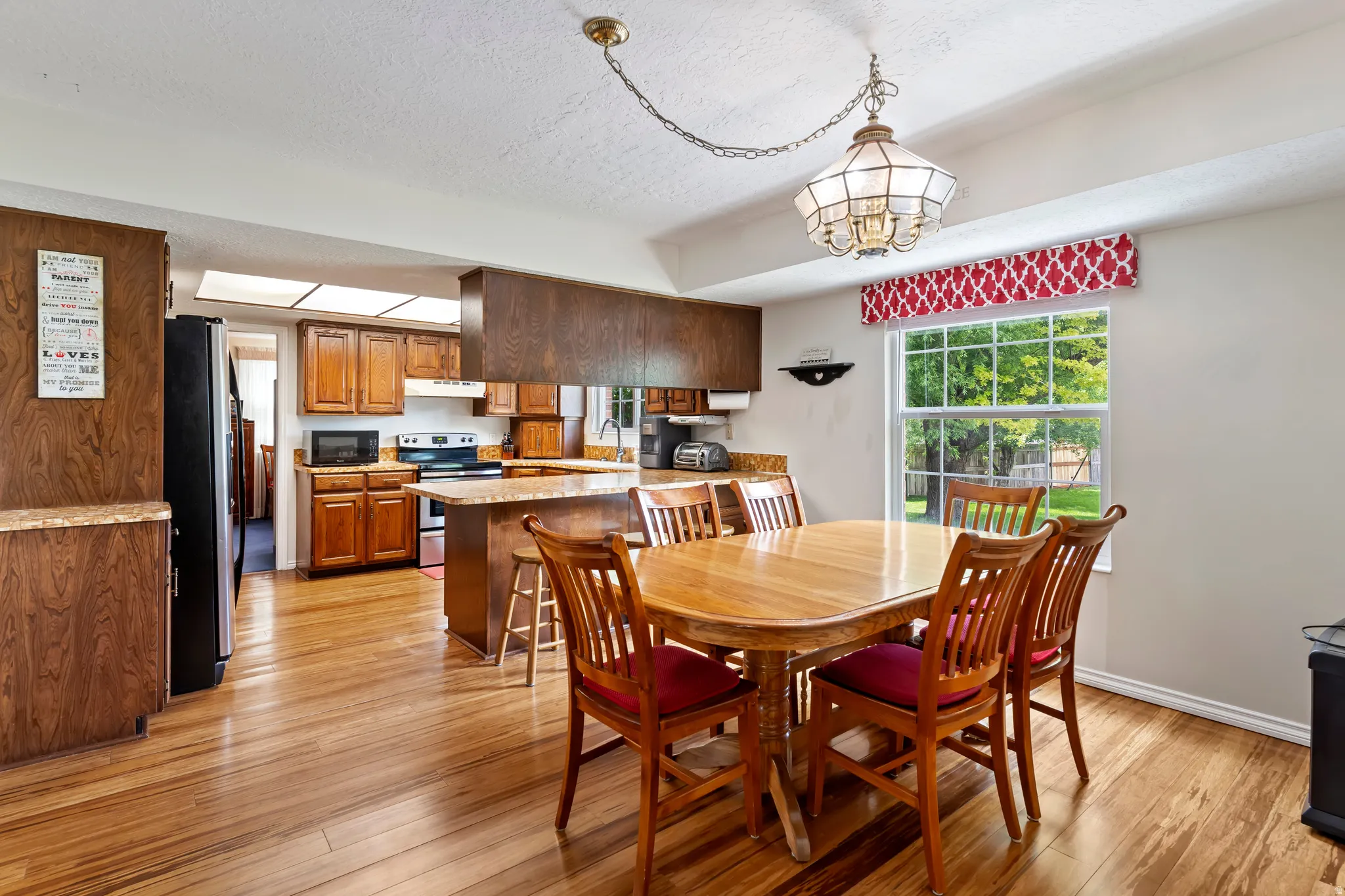 Open-concept kitchen and dining area featuring wood-finish flooring, recessed lighting, and a large window overlooking exterior greenery