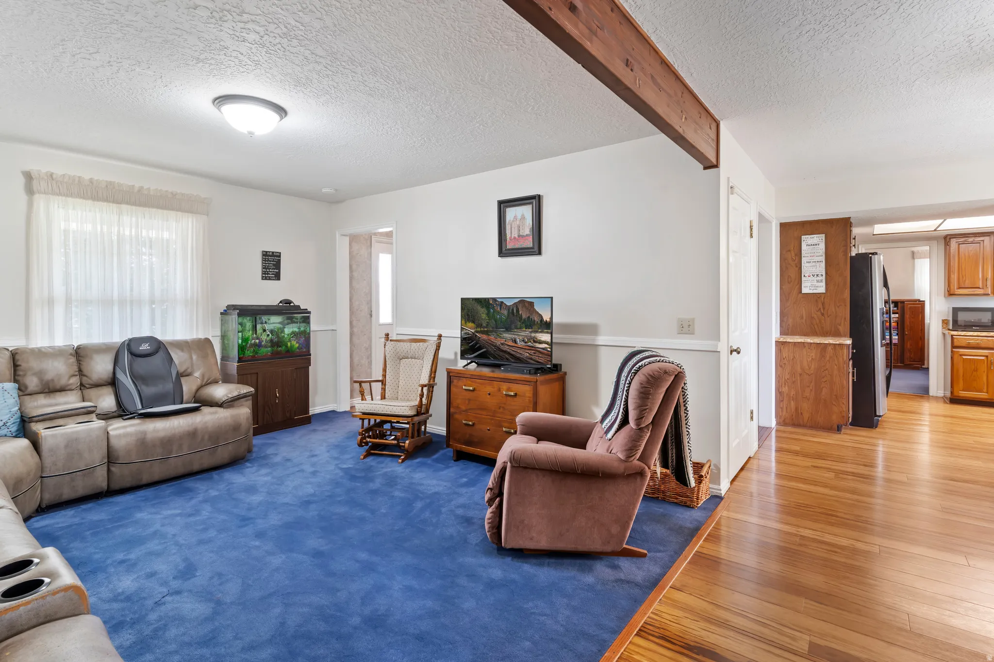Living area featuring blue carpet, a textured ceiling, and a prominent wood beam