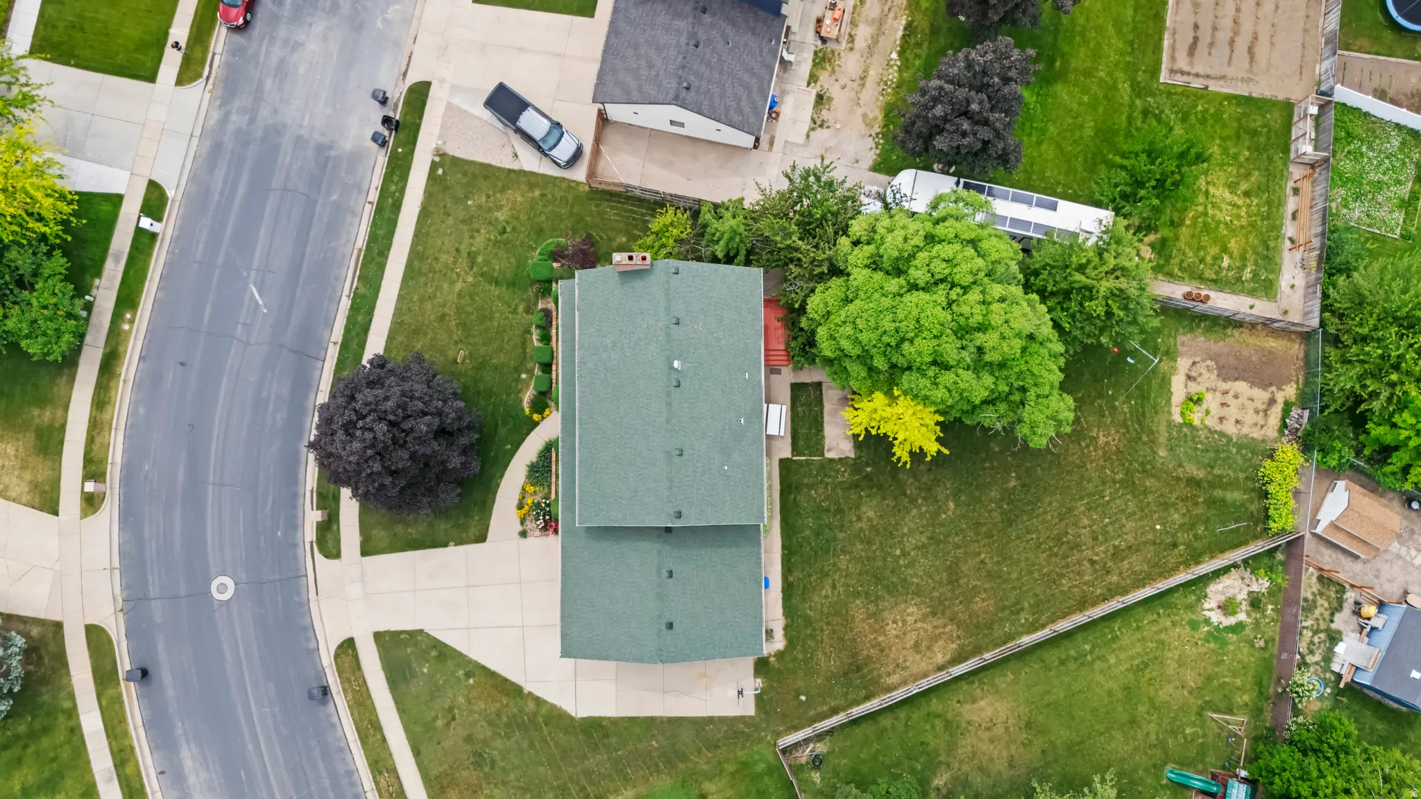 Property featuring a green shingle roof, established landscaping, and a curvilinear paved street