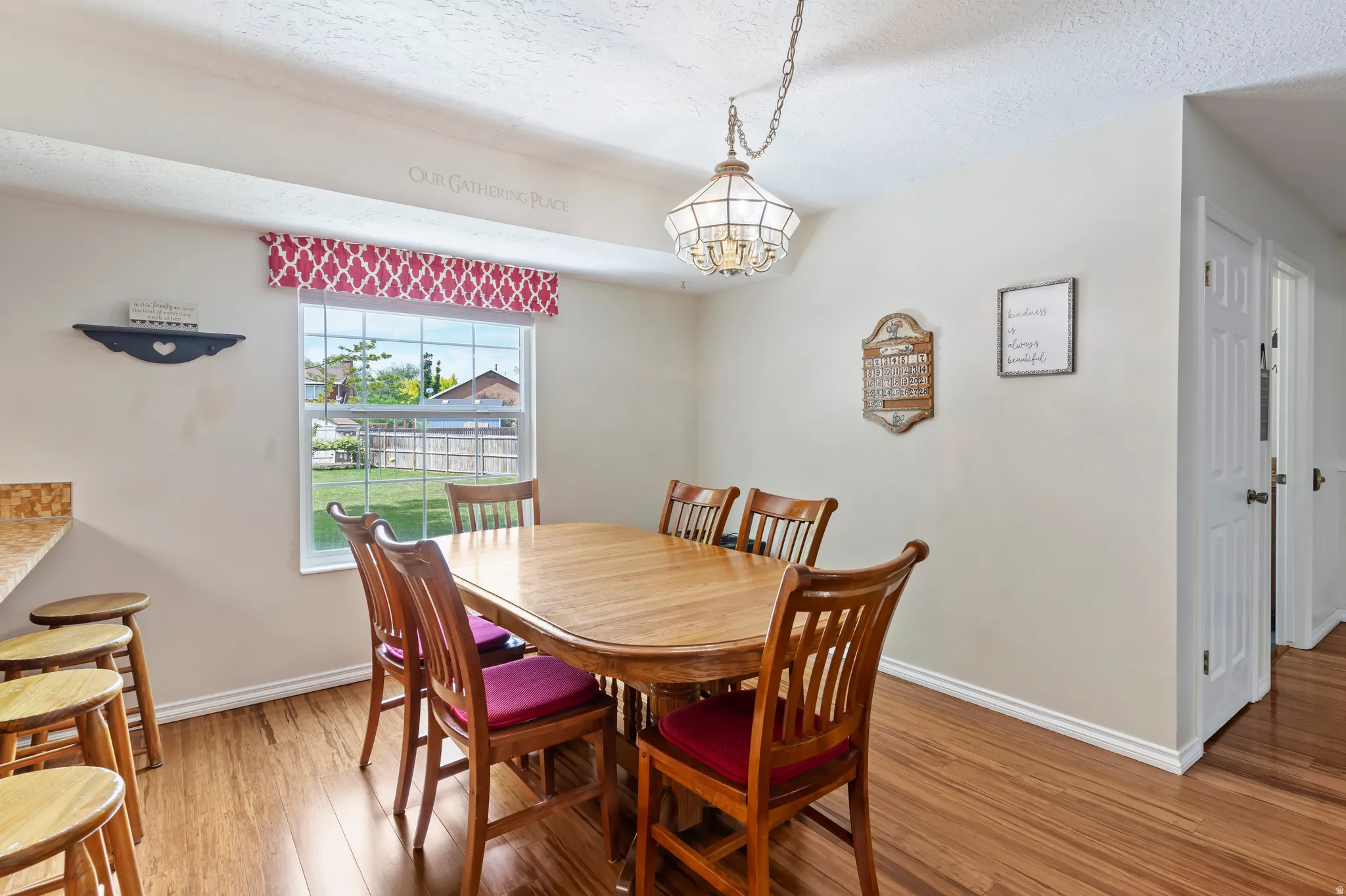 Dining area featuring wood-finish flooring, a window overlooking the backyard, and a decorative ceiling light fixture