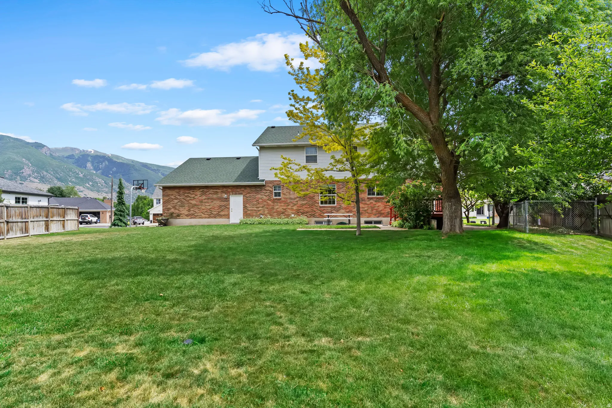 Expansive backyard featuring a manicured lawn, mature trees, and a wooden privacy fence