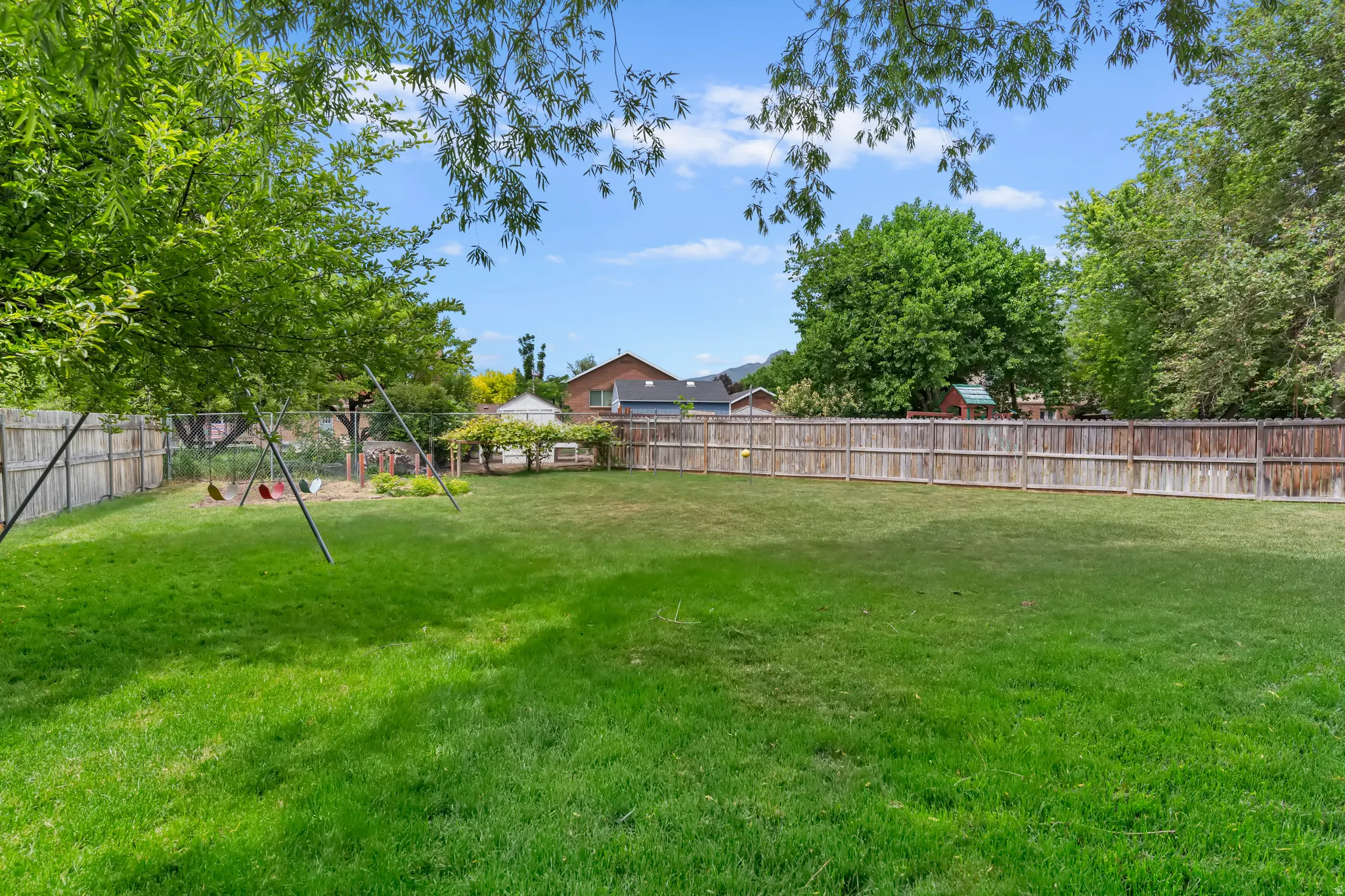 Expansive backyard featuring a lush green lawn, full privacy fencing, mature trees, and a dedicated garden area