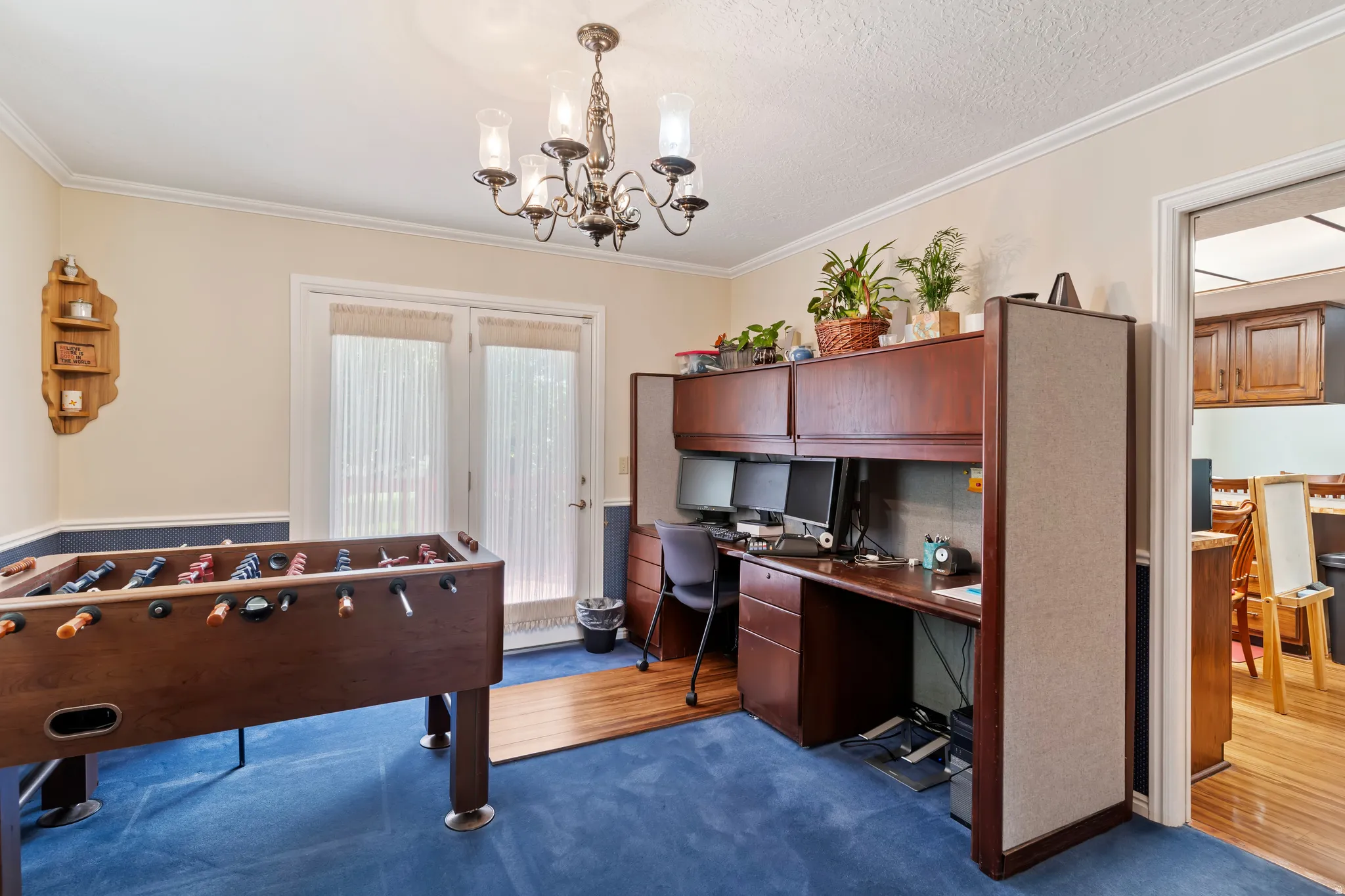 Versatile room featuring a built-in office workstation with overhead cabinetry, crown molding, and direct access to the outdoors via double french doors