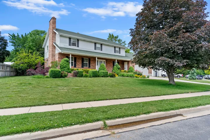 Two-story residence featuring brick and siding facade, a prominent front porch, and mature landscaping