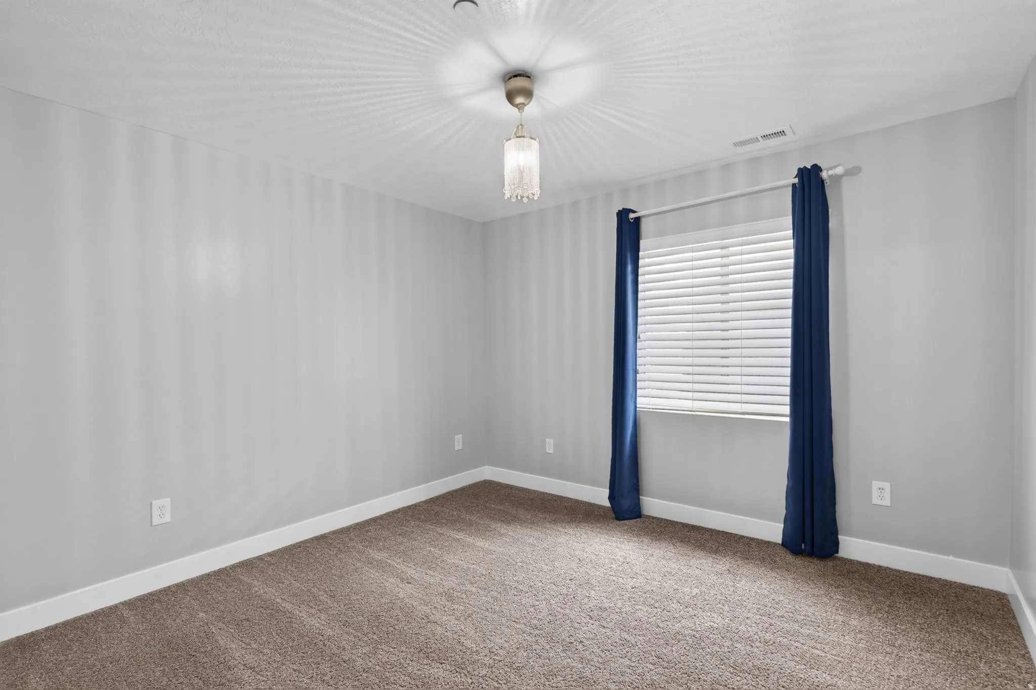 Basement Bedroom 2 of 3. Carpeted room featuring a window with horizontal blinds, light gray wall paint, white baseboards, and a ceiling-mounted light fixture