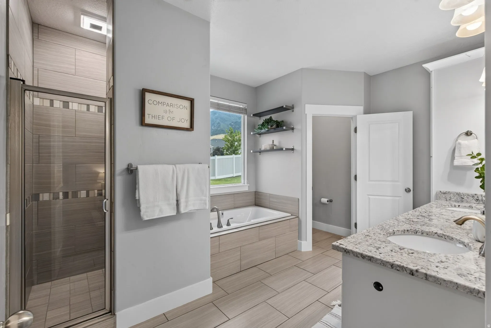 Spacious master bathroom featuring a glass-enclosed shower, a large soaking tub with tile surround, and a vanity with granite countertop
