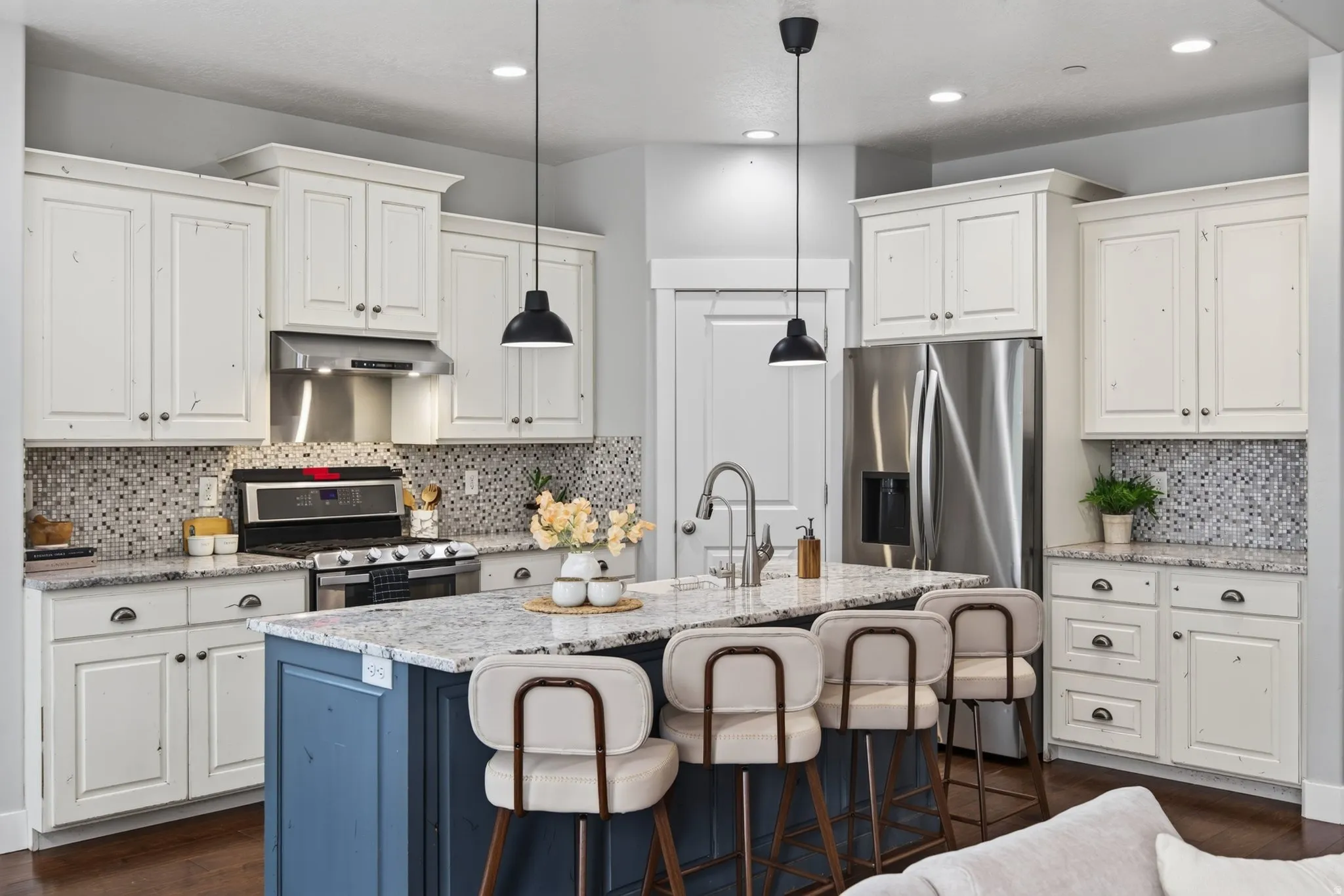 Bright kitchen with granite countertops, large island seating, white cabinetry, stainless appliances, farm sink, and range hood vented outside.