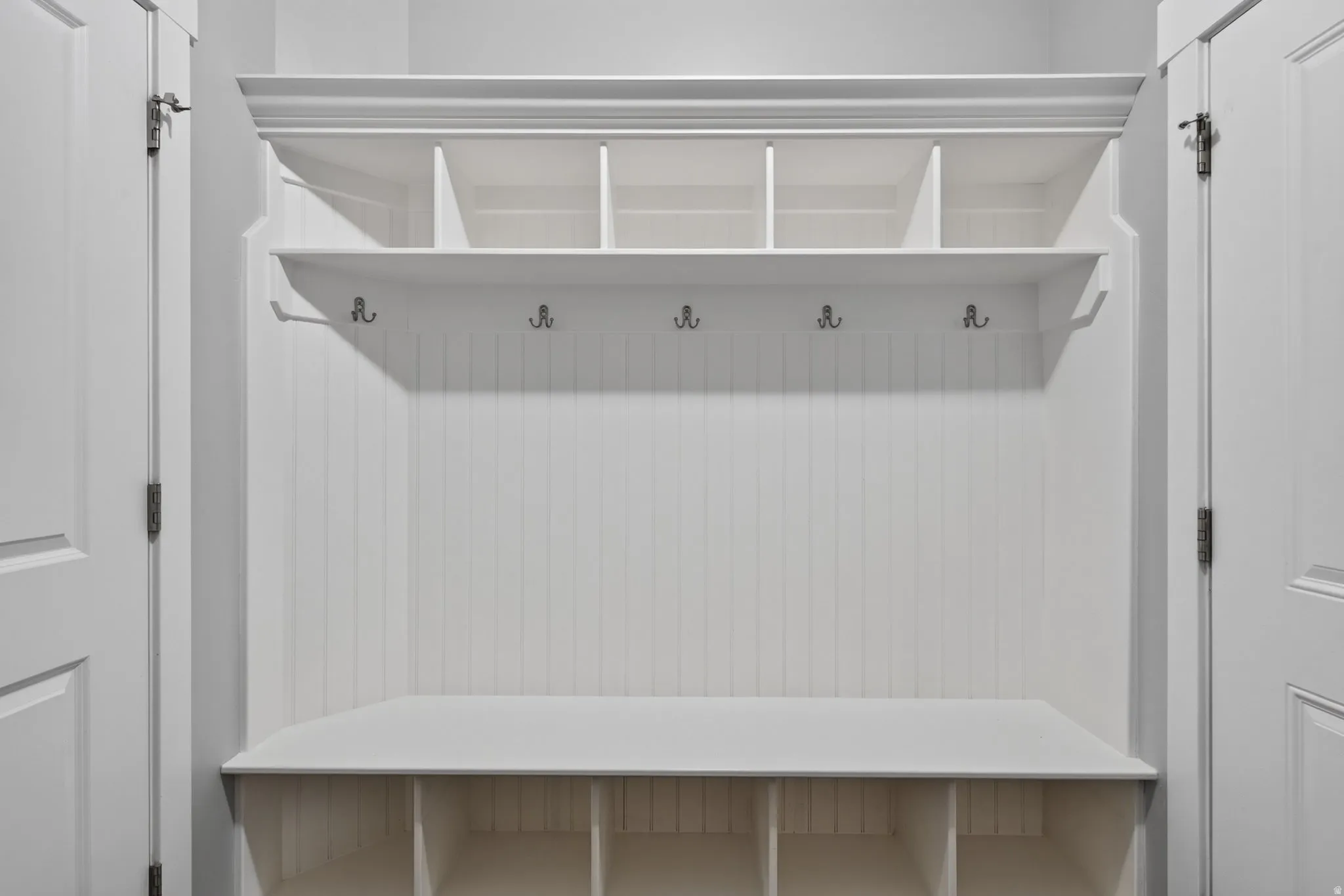 Main level mud room/laundry room with door to garage. Built-in white storage unit featuring beadboard paneling, upper cubbies, coat hooks, a bench, and lower storage compartments
