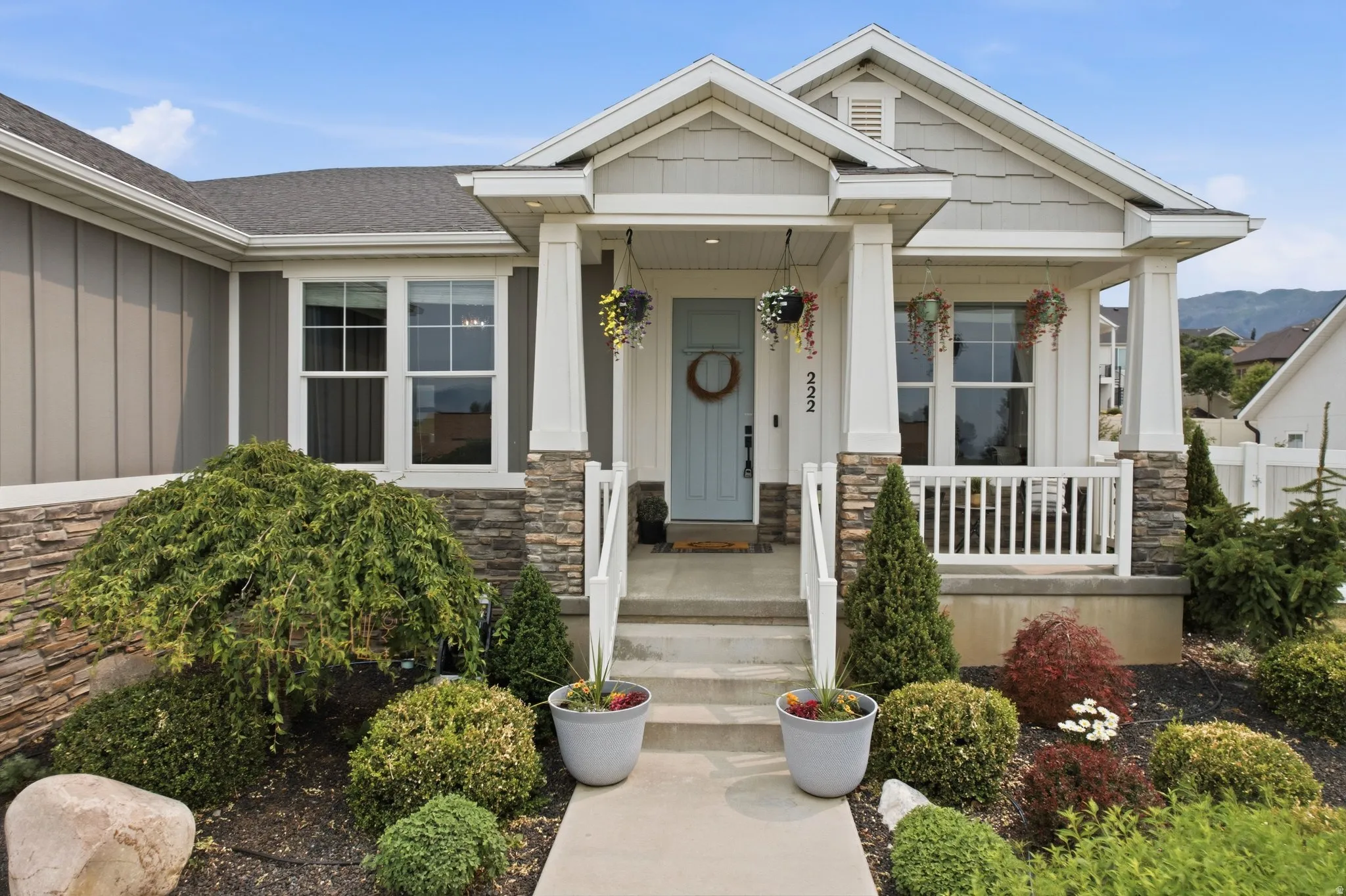 Welcoming entry with a covered porch featuring stone-clad columns and a light blue paneled front door