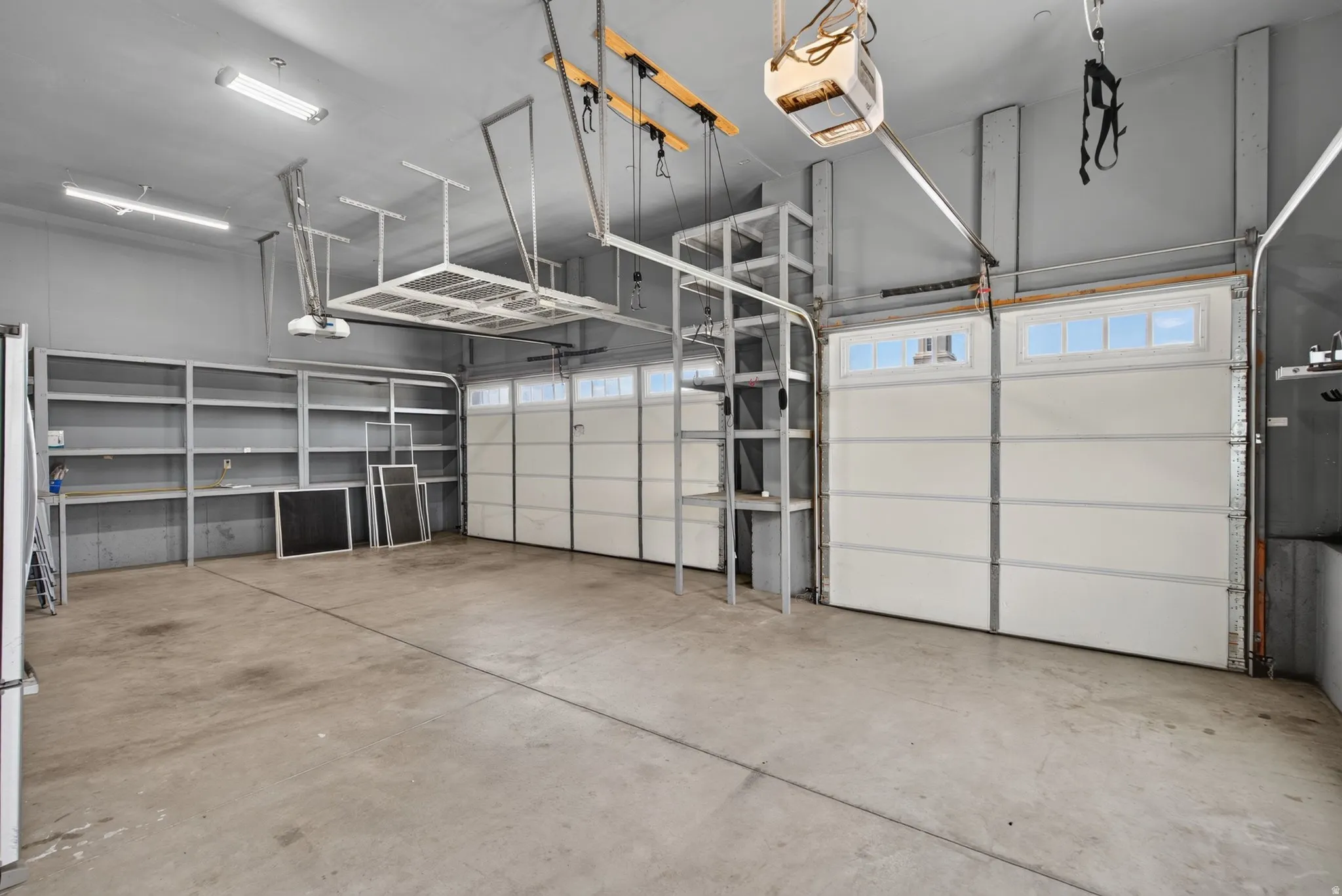 HUGE Spacious garage featuring two overhead doors with window accents, TONS of built-in shelving, overhead storage racks, and concrete flooring