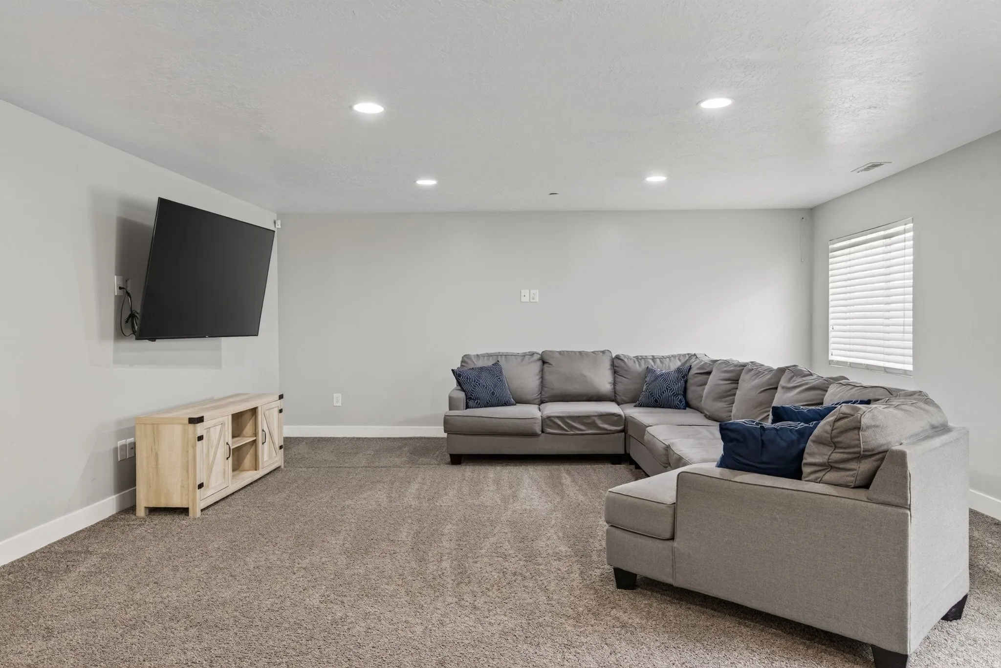 Spacious finished basement family room with recessed lighting, neutral carpet, wall-mounted TV area, and plenty of room for movies, games, or relaxing.