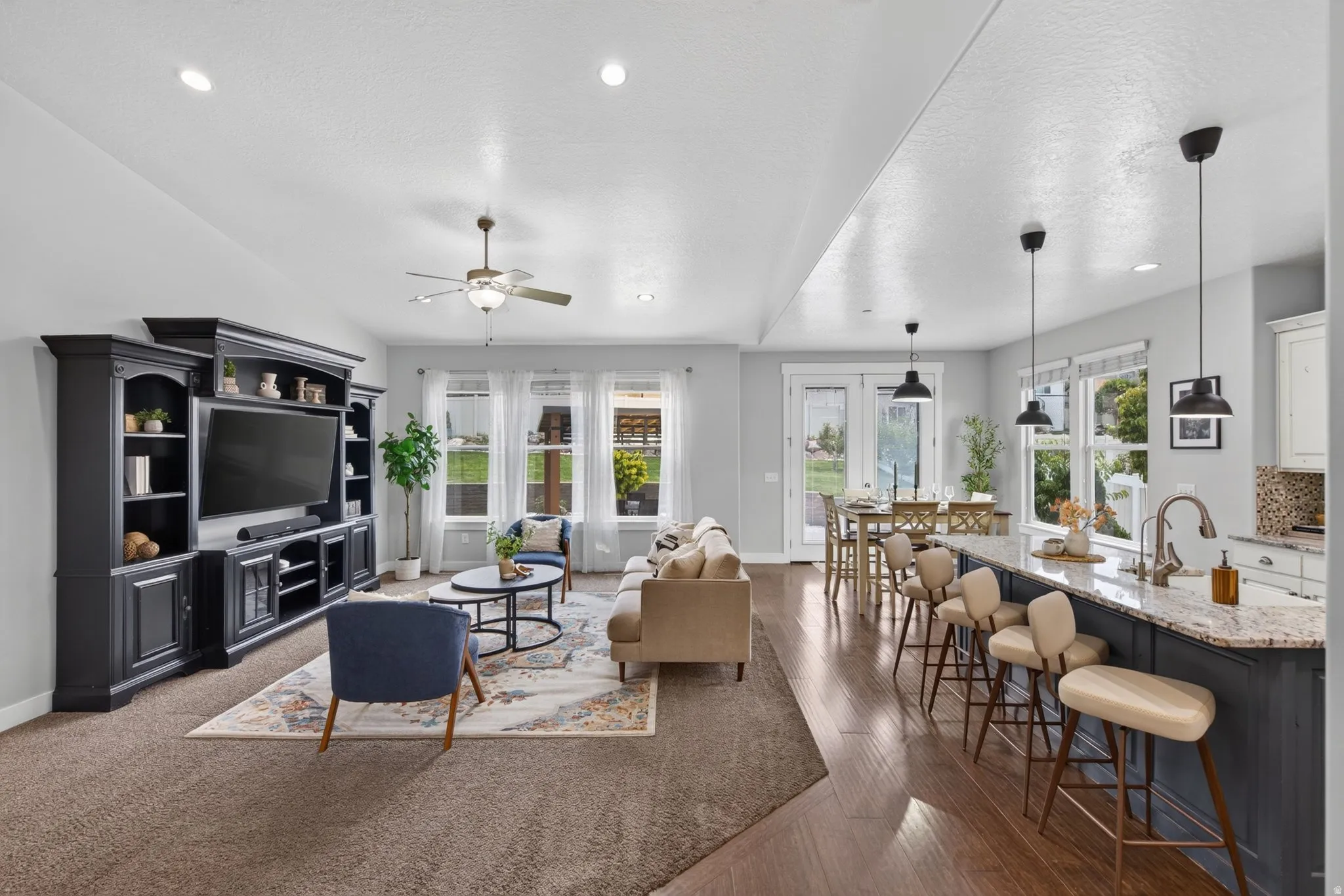 Bright open-concept main living area with kitchen, dining, island seating, built-in entertainment center, abundant natural light, and backyard views.