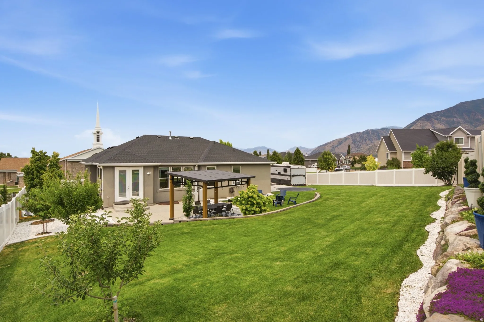Spacious backyard featuring an extensive lawn, white vinyl fencing, and mountain backdrop