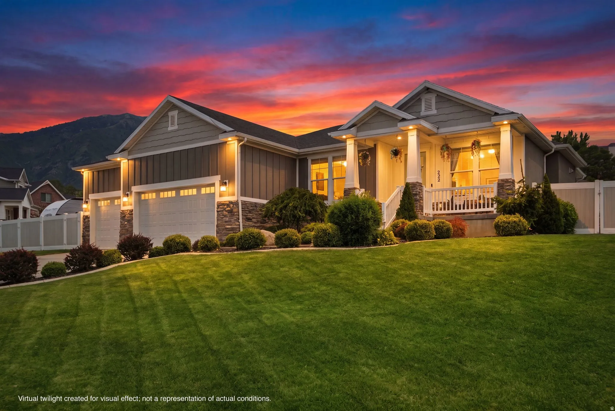 Twilight exterior showcasing warm curb appeal, architectural lighting, covered front porch, manicured lawn, and peaceful mountain setting.