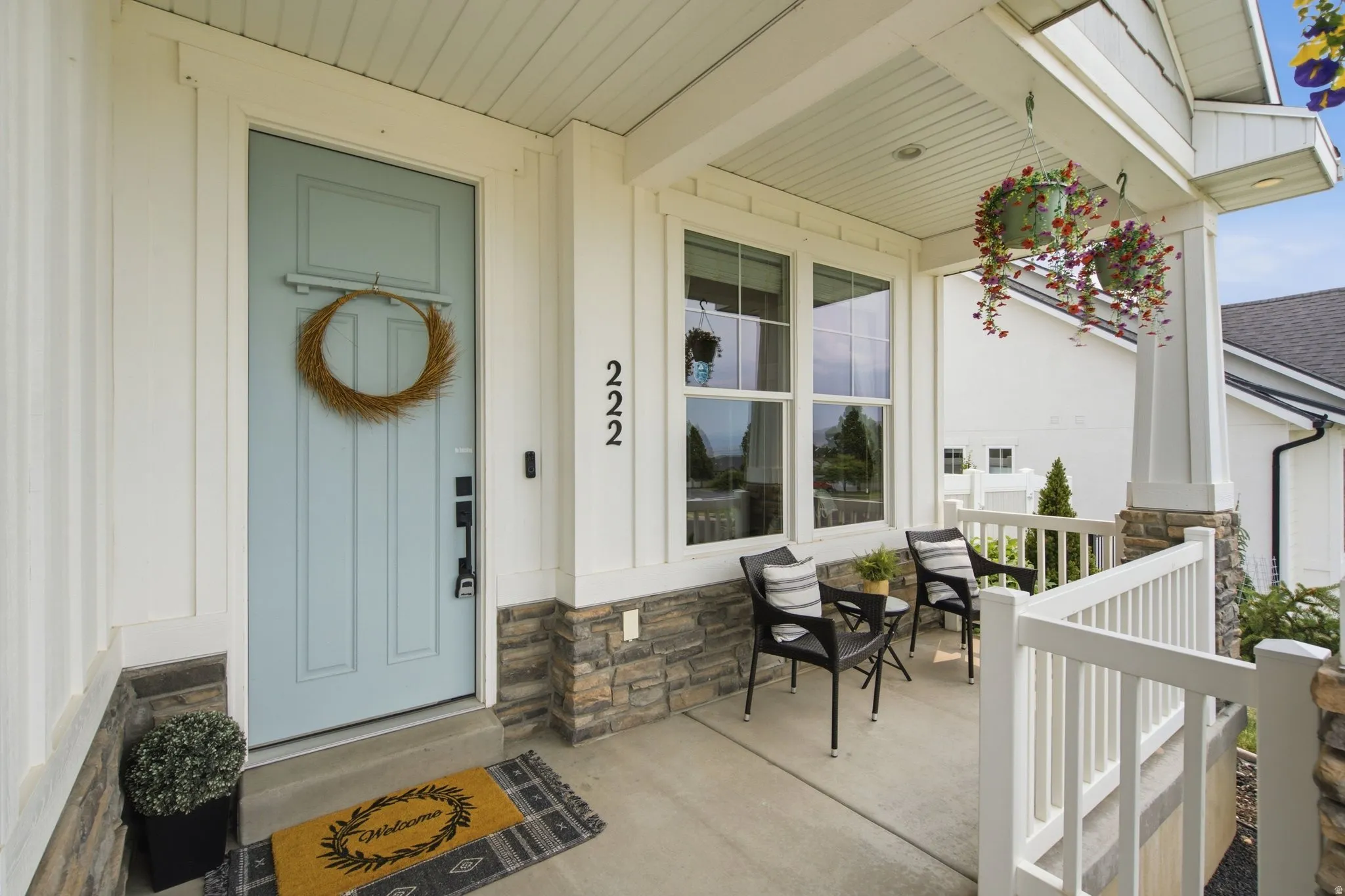 Inviting front porch featuring a light blue entry door, white vertical siding, stone veneer accents, and a white railing