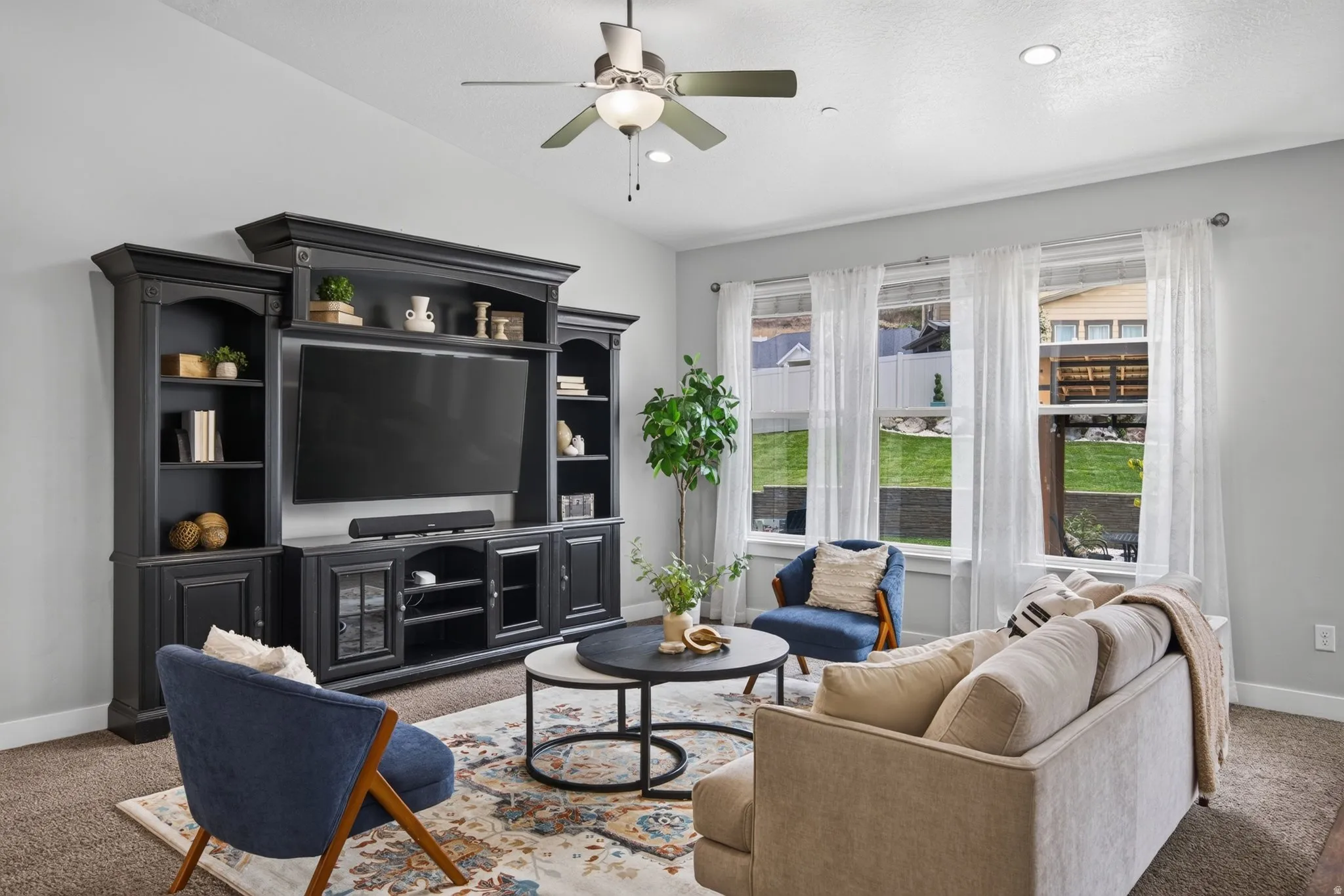 Comfortable main-level living room with built-in entertainment center, large windows, backyard views, and a bright open connection to the kitchen and dining areas.