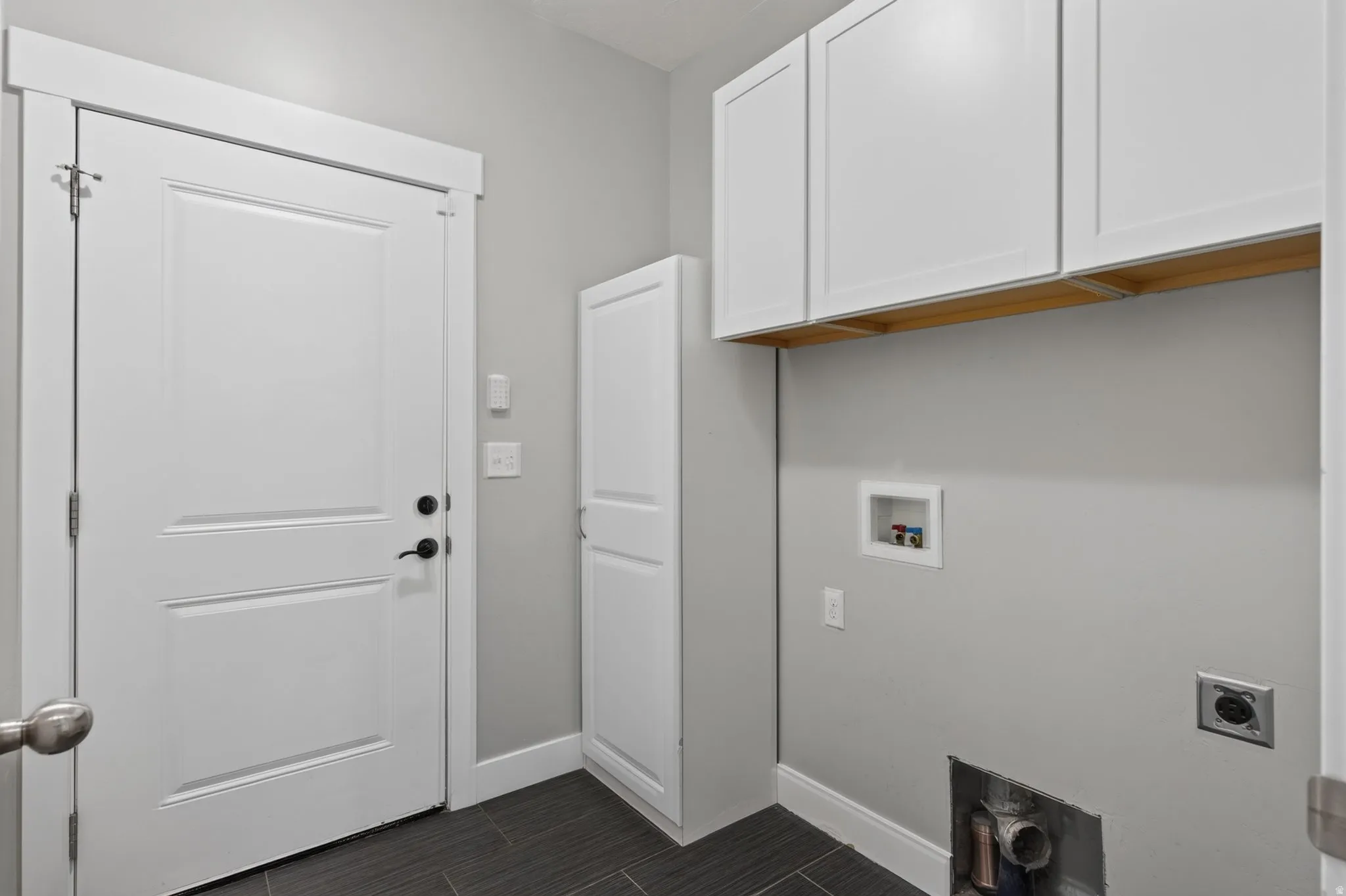 Laundry on the main level with door to the garage - featuring white shaker-style cabinetry, dark tile flooring, and a white paneled door with dark hardware
