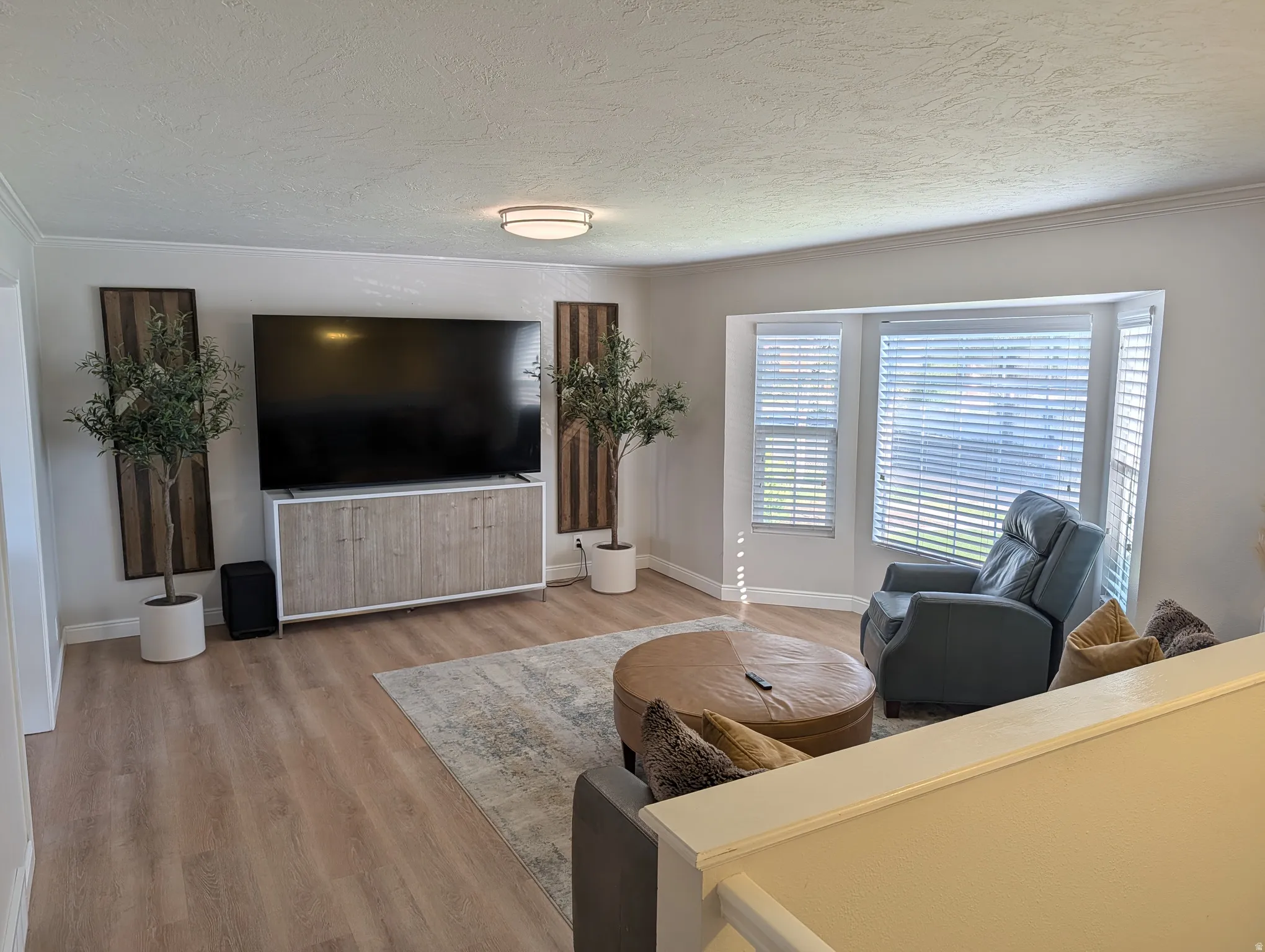 Living area with light-toned wood-finish flooring, a contemporary ceiling light fixture, and crown molding