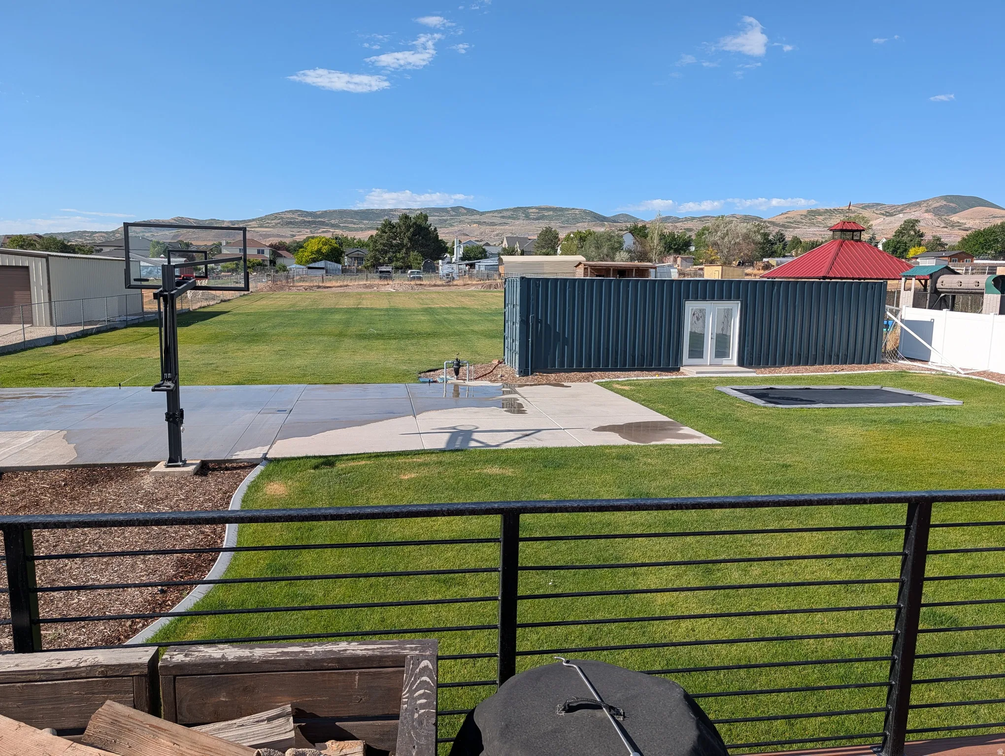 Expansive outdoor area featuring a basketball hoop on a concrete pad, a shipping container structure with double doors, and a sunken trampoline