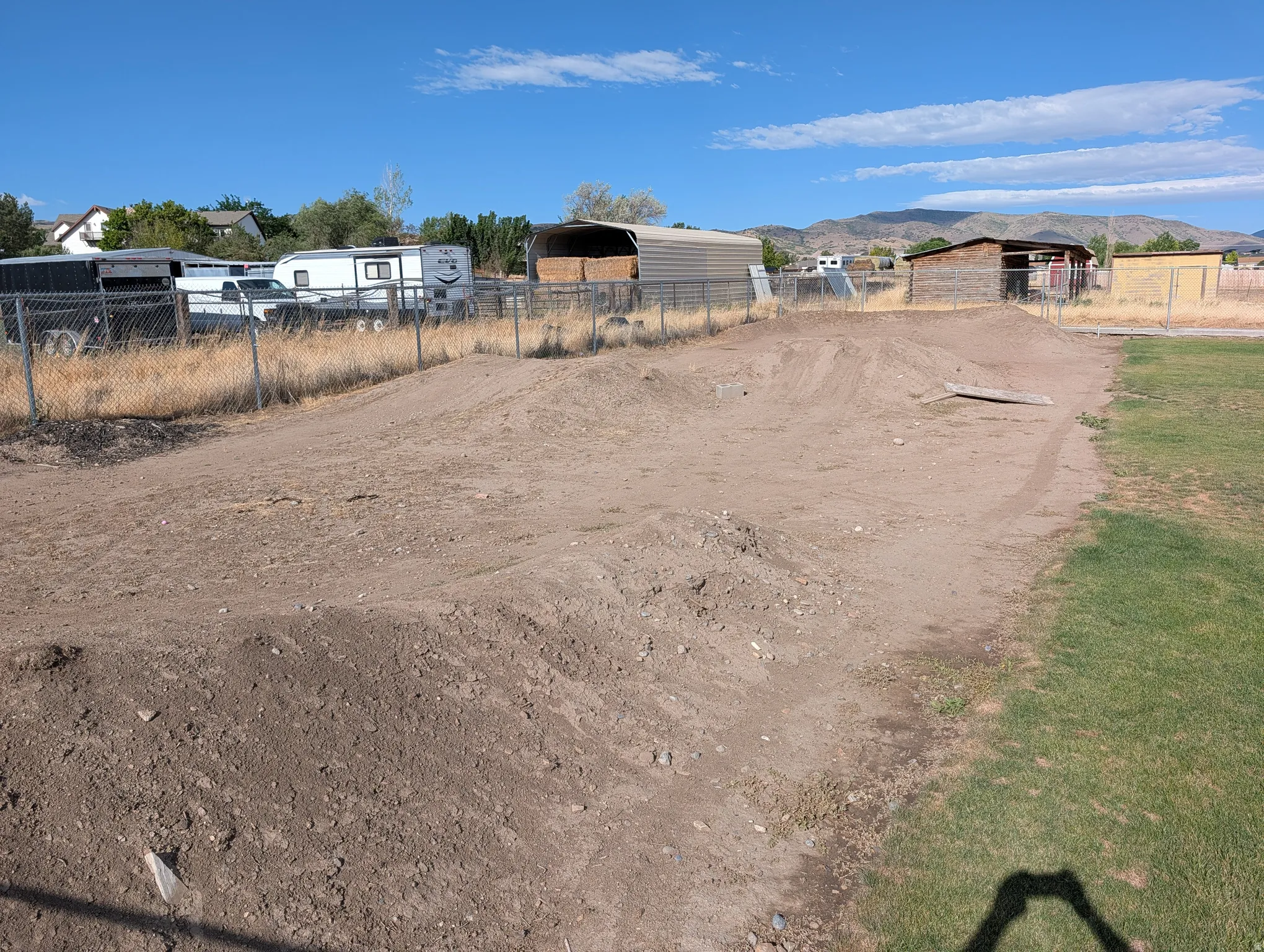 Dirt bike track. Expansive outdoor area featuring a dirt track with multiple mounds and a bordering chain-link fence