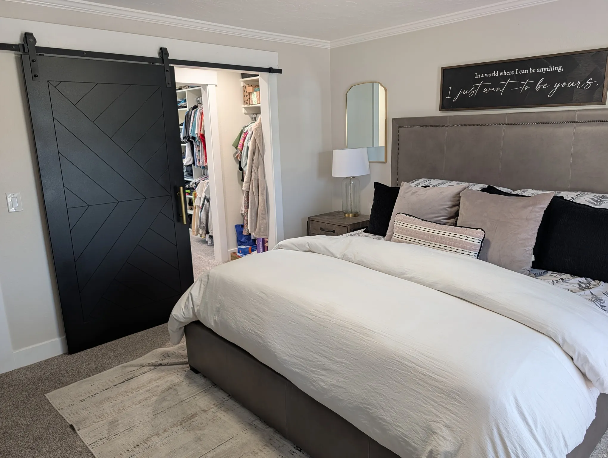 Bedroom featuring a dark barn door with geometric paneling, opening to a walk-in closet with built-in shelving and hanging rods