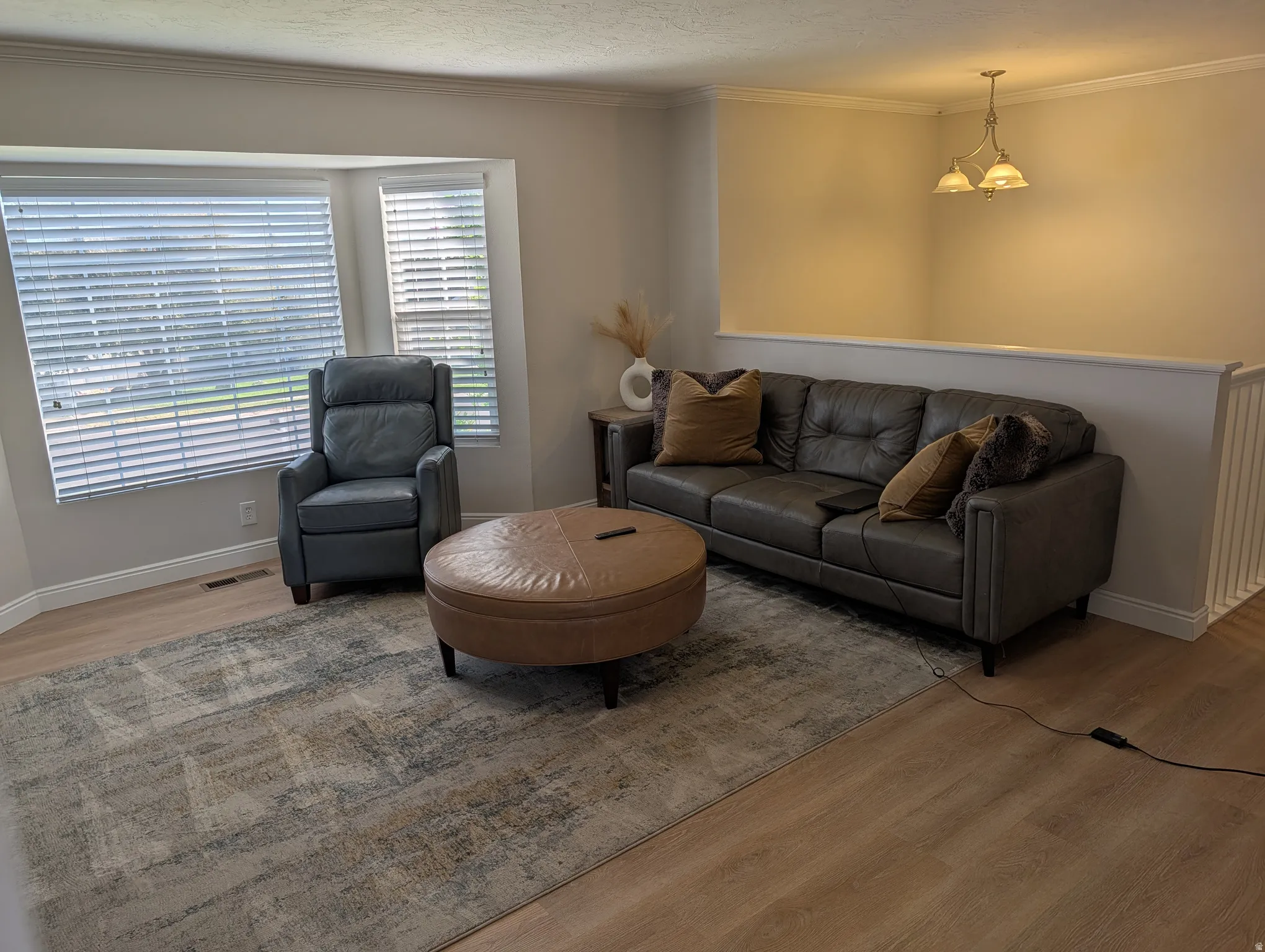 Bright living area featuring light wood-finish flooring, a bay window with blinds, and white baseboards